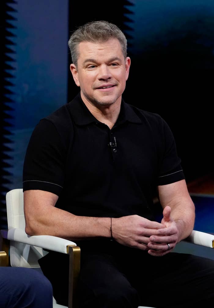 A person sits in a chair during an interview, wearing a casual black polo shirt