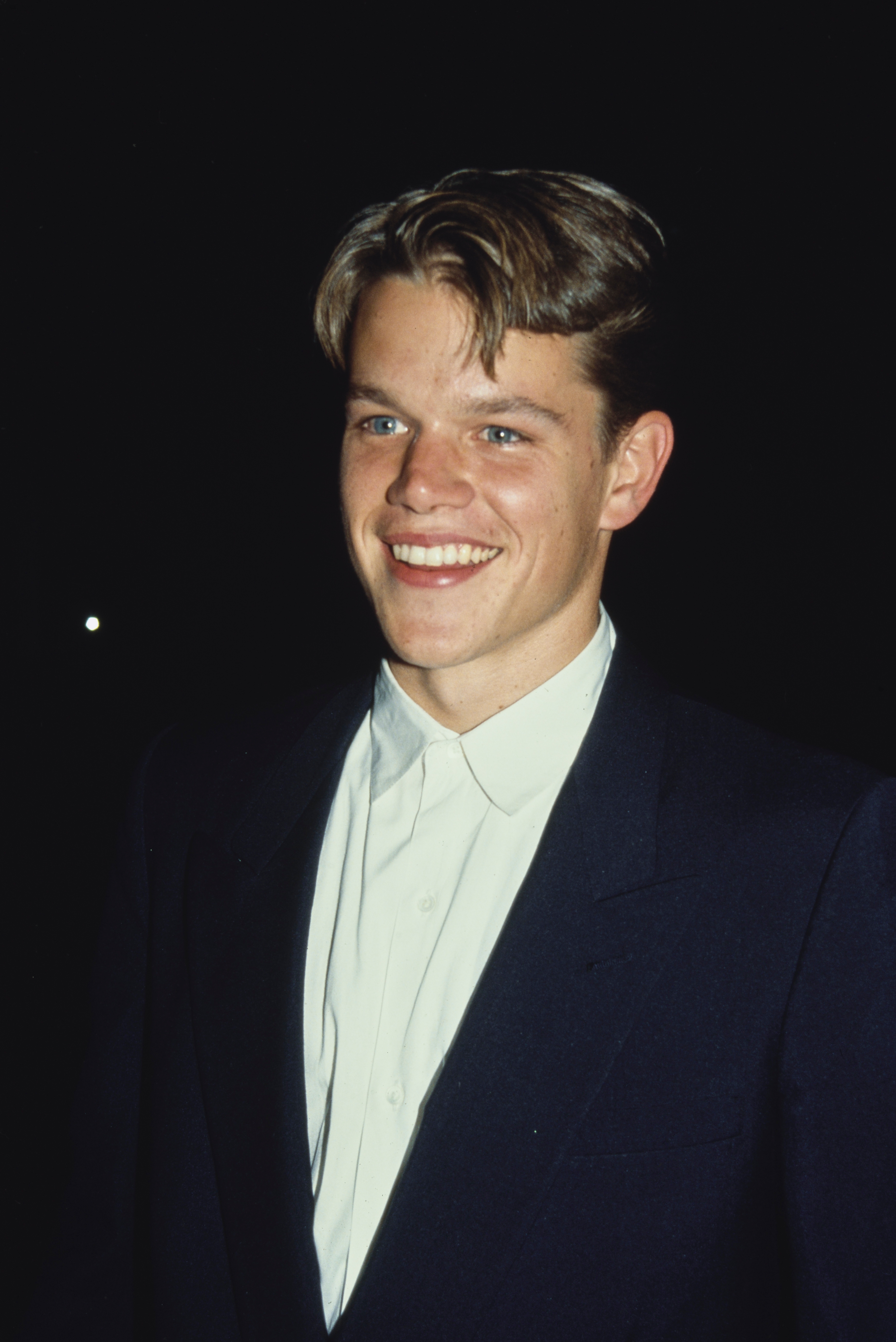 A person in a suit with a white shirt smiles at an event