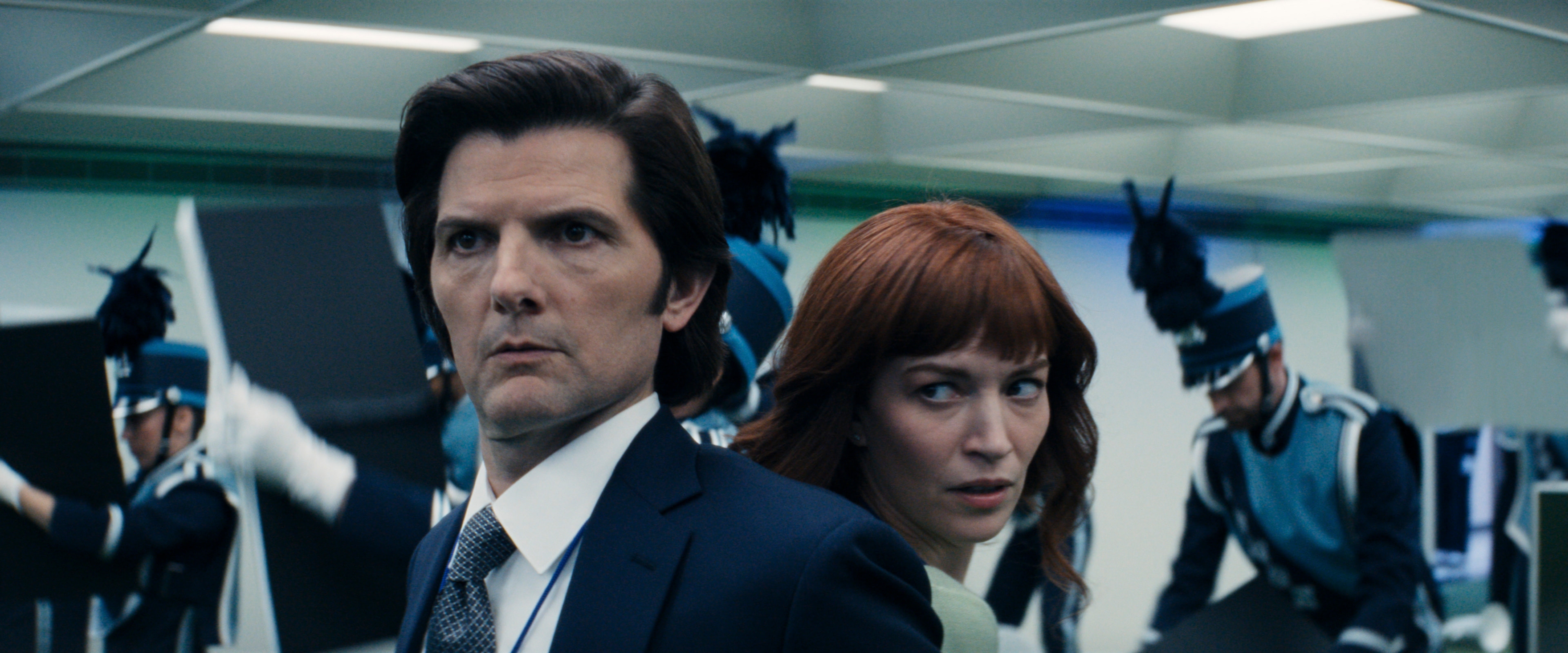 Two characters successful  concern  attire look   tense portion    a marching set  performs successful  the background. Scene appears melodramatic  and cinematic