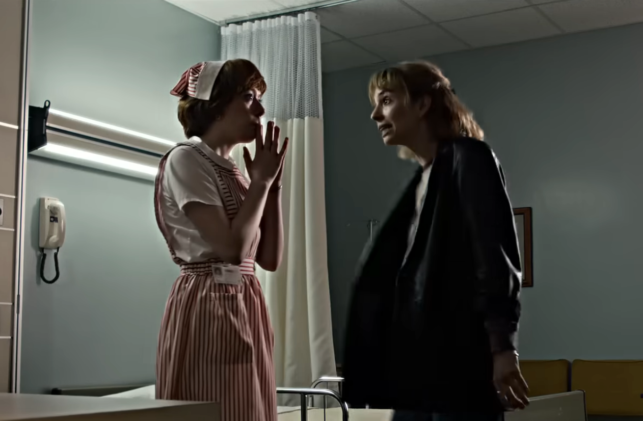 Two individuals in a hospital room, one in a retro nurse uniform, appear engaged in a tense conversation