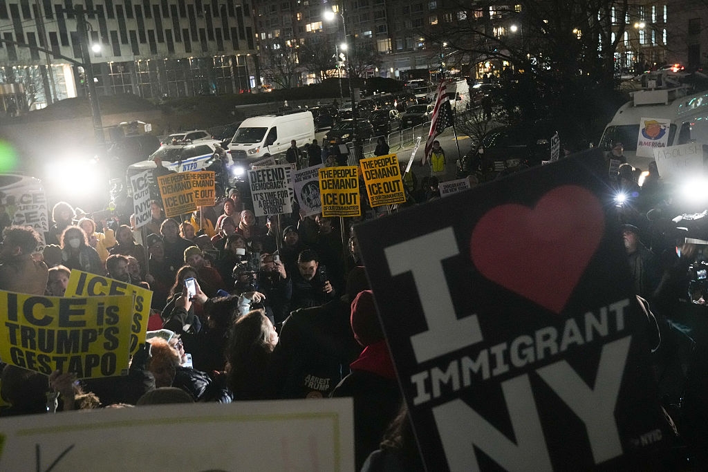 Demonstranter om natten holder skilt med meldinger som støtter innvandrere og kritiserer ICE