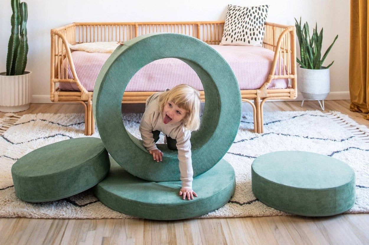 Child playing with large, circular, foam blocks in a stylish, modern living room with a wooden sofa and plants for sale
