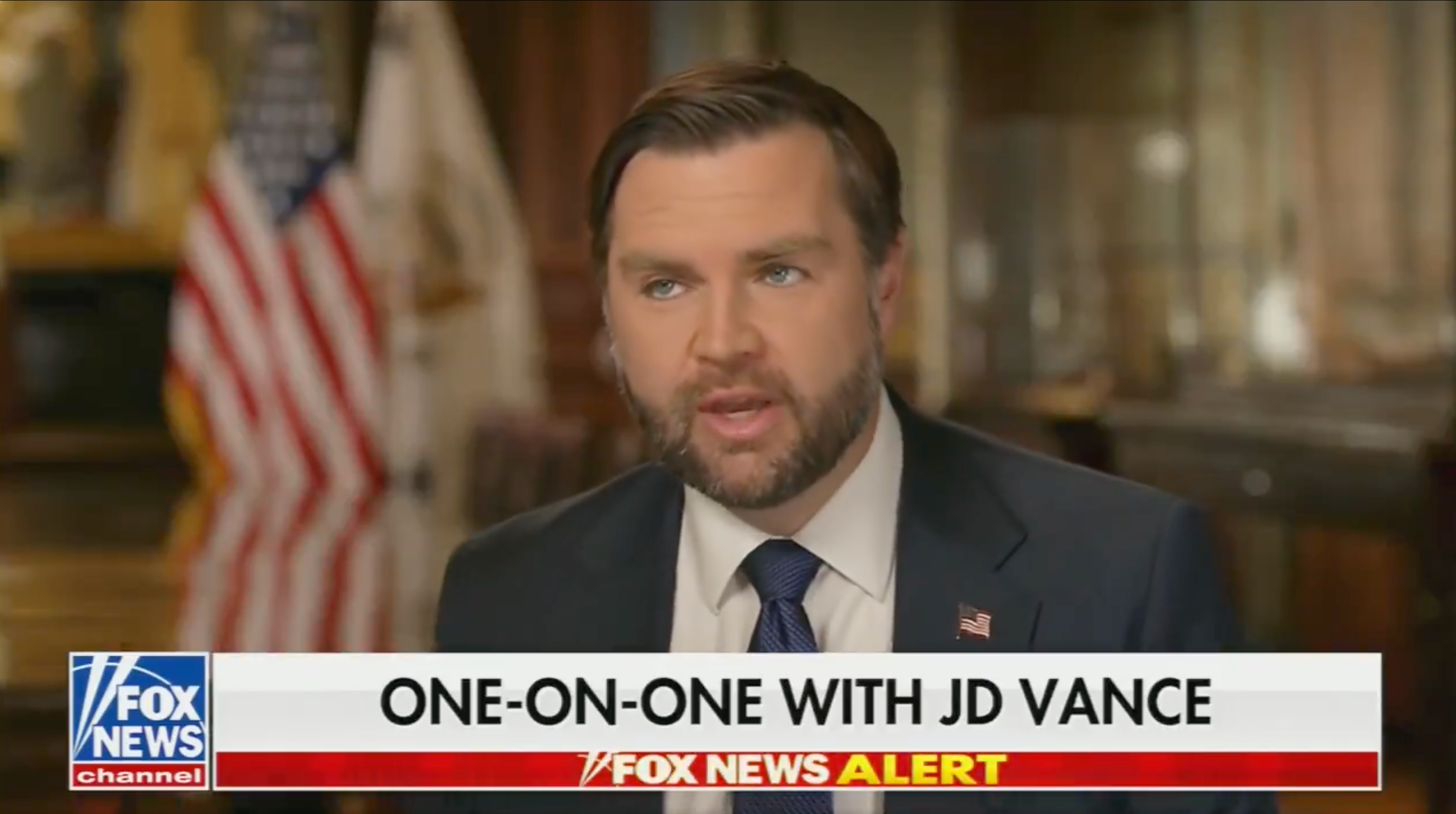 Mann i dress snakker i et TV-intervju merket 