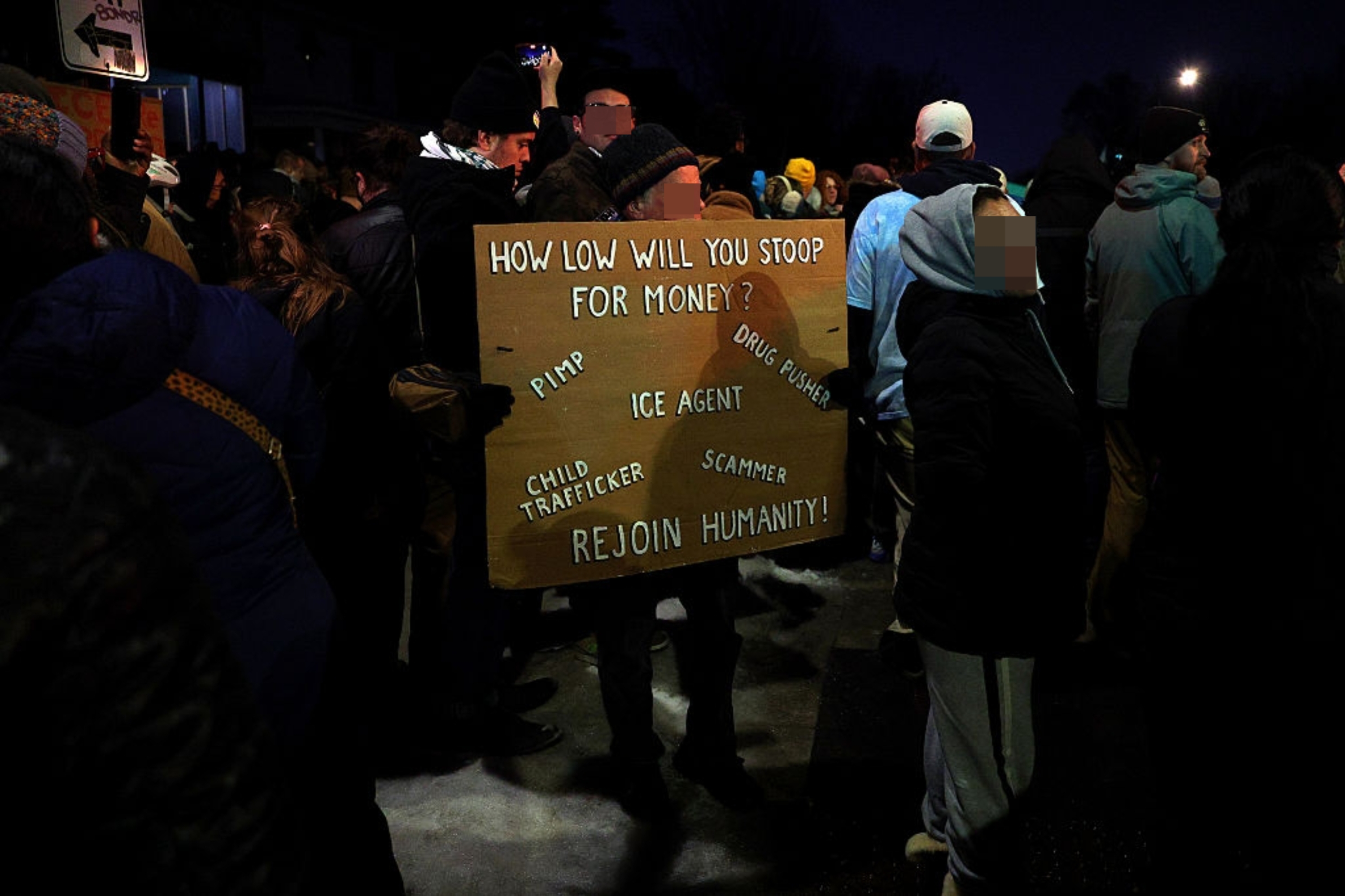 En folkemengde protesterer om natten. Et fremtredende skilt lyder: 