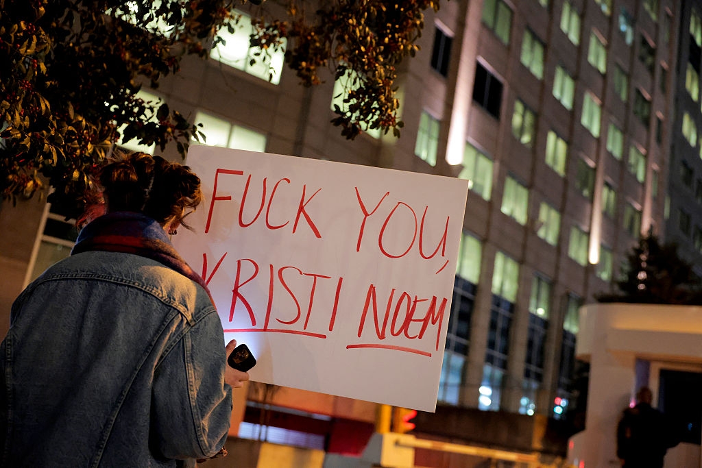 Person som holder skilt med kritisk melding rettet mot Kristi Noem i urbane omgivelser