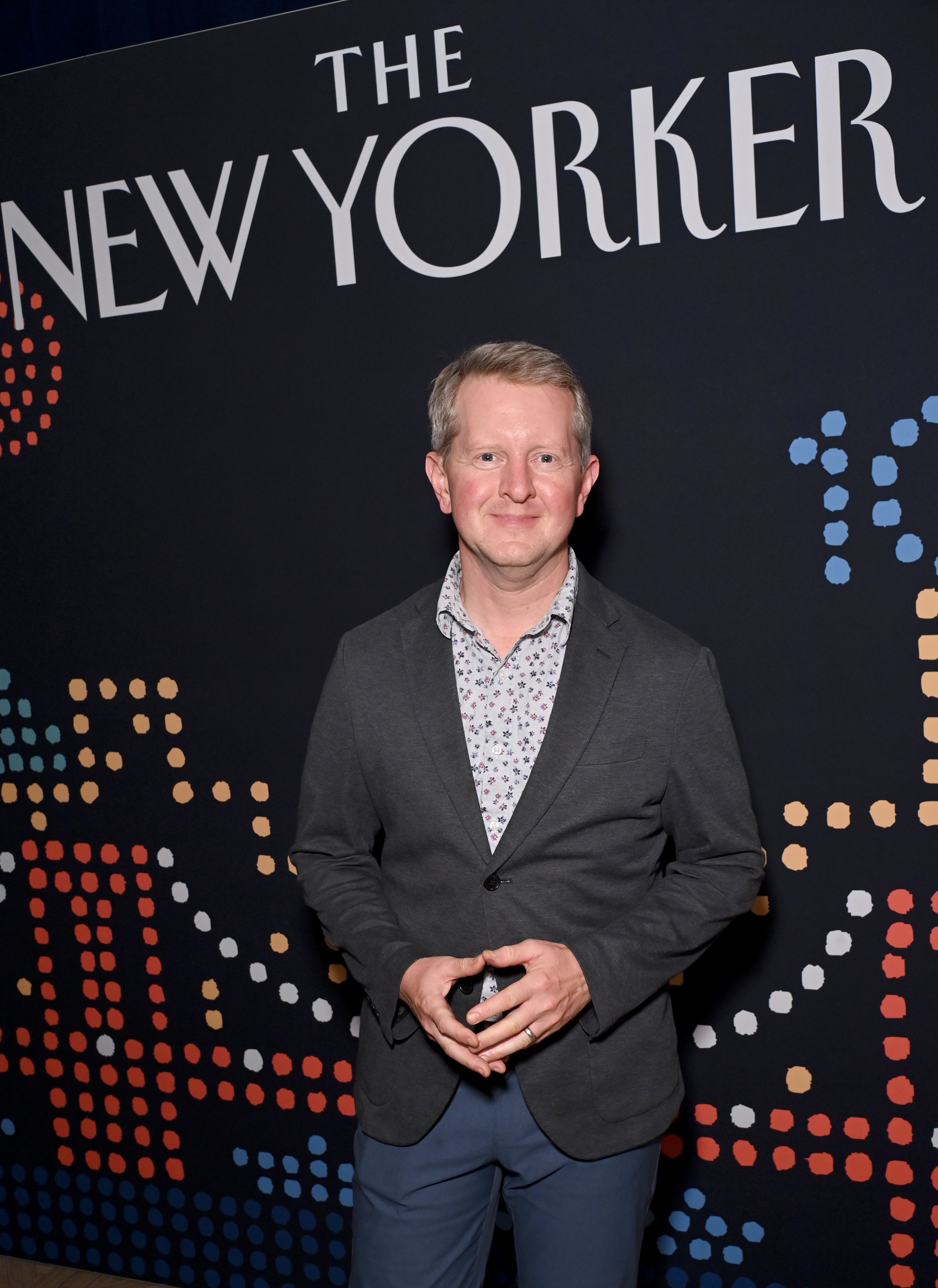 Ken Jennings in a patterned shirt and blazer stands before a "The New Yorker" backdrop at an event
