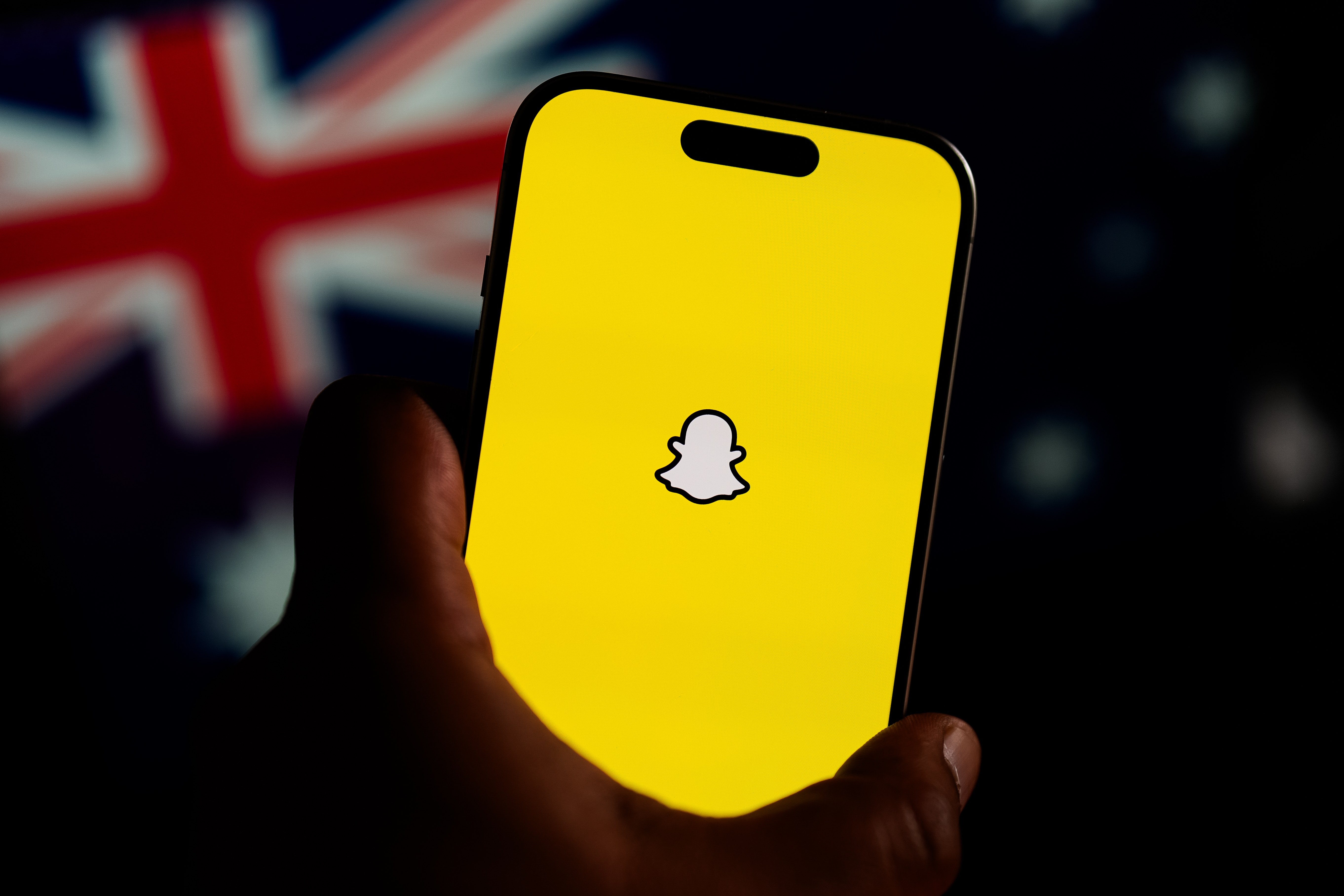 En hånd holder en smarttelefon som viser Snapchat-logoen, med et australsk flagg uskarpt i bakgrunnen
