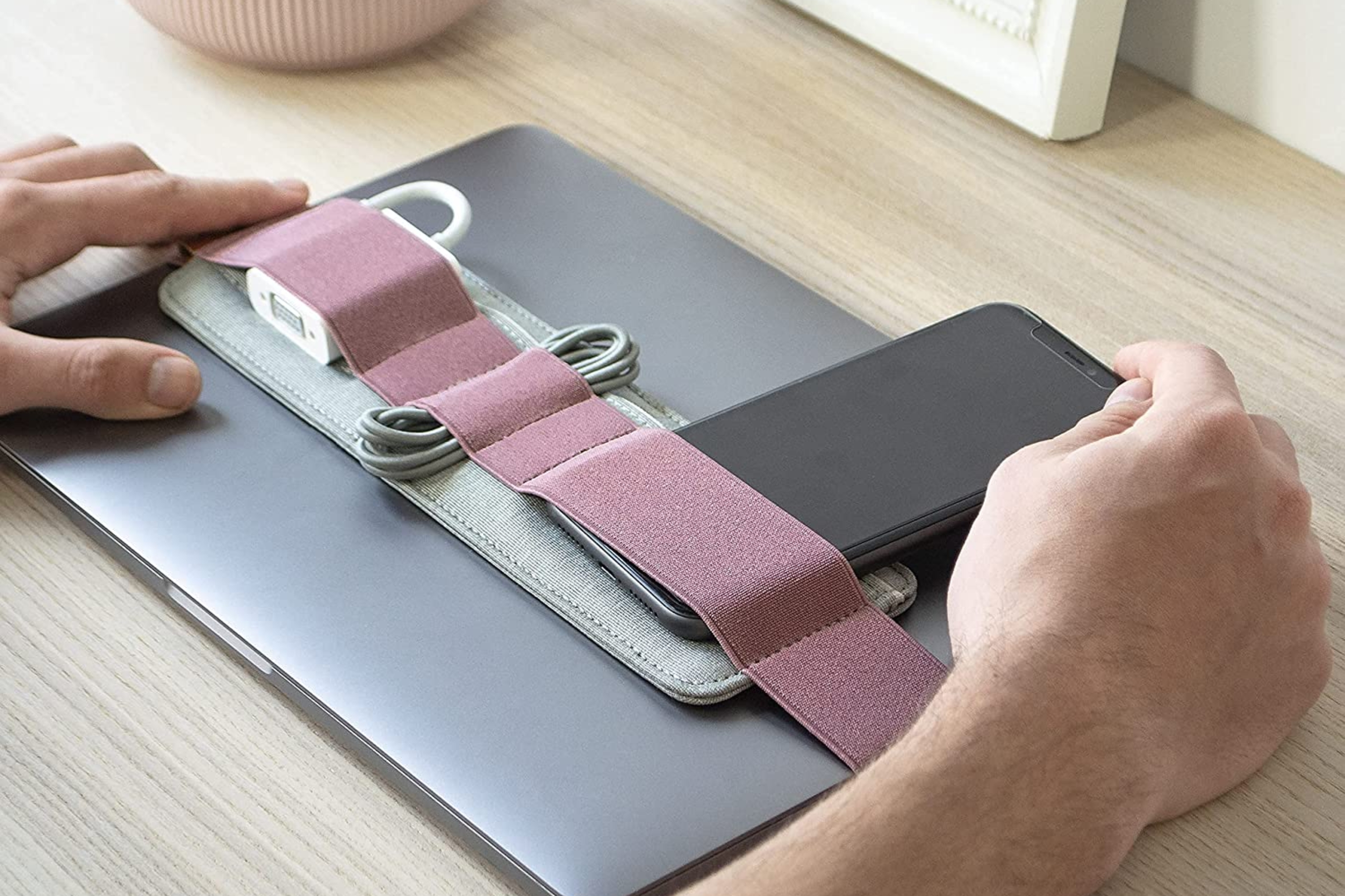 A pink elastic belt around a laptop holding a phone, a charger, and cords 