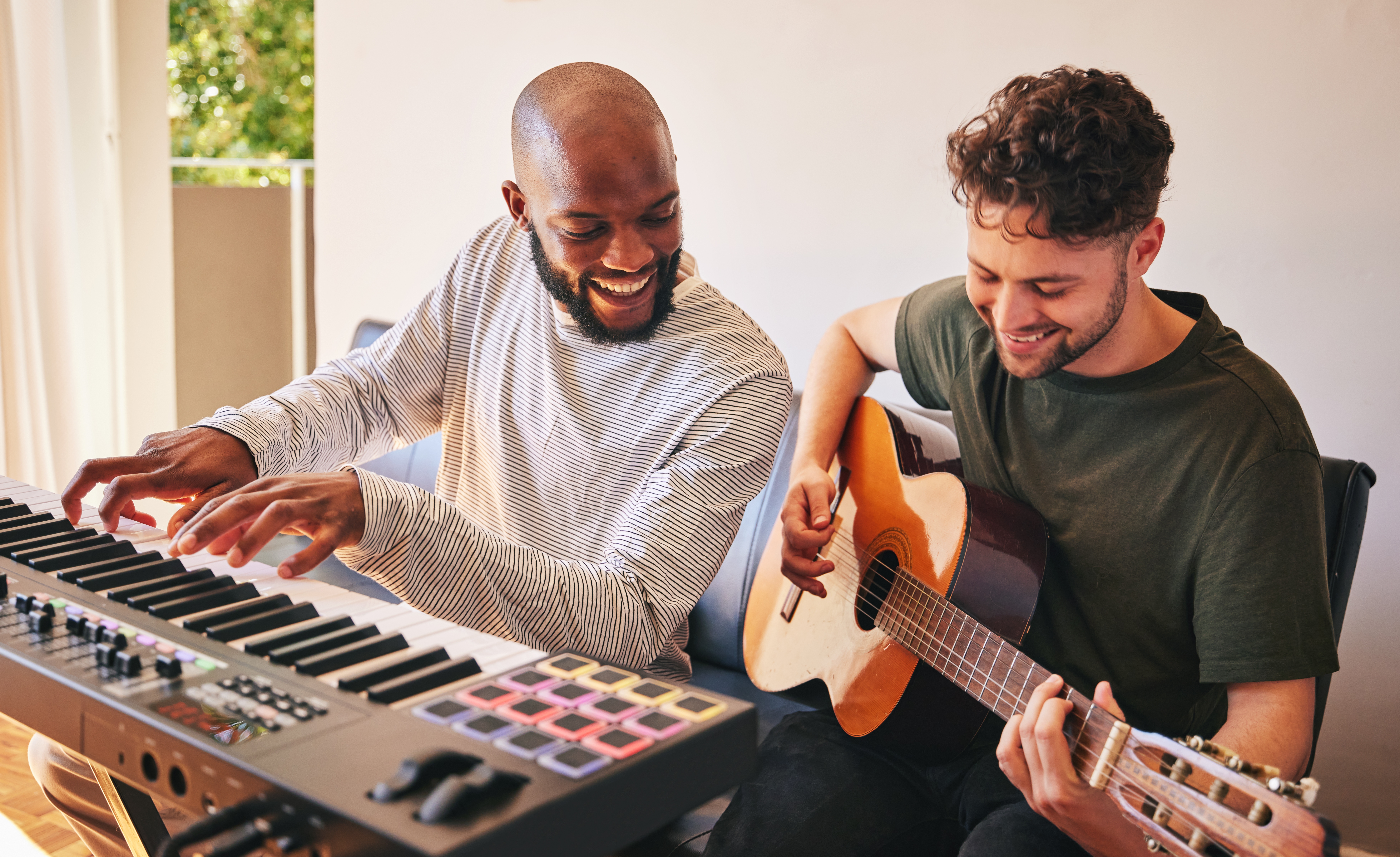 Two radical   joyfully making euphony  together; 1  plays the keyboard, the different   plays the guitar. They are indoors, smiling and engaged