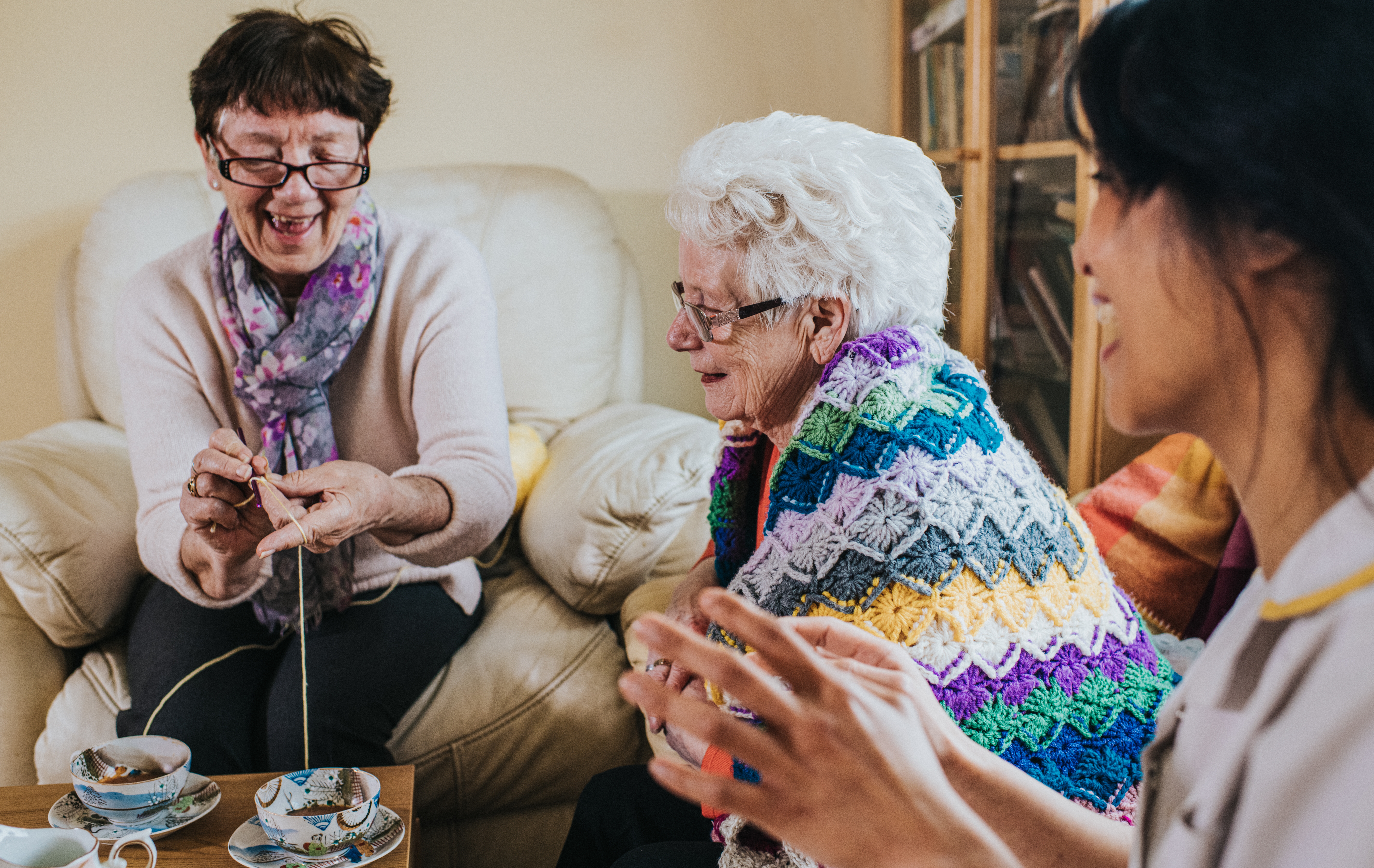 Two aged  women and a caregiver bask  a crafting league   with yarn and tea, sharing smiles and speech  successful  a cozy setting
