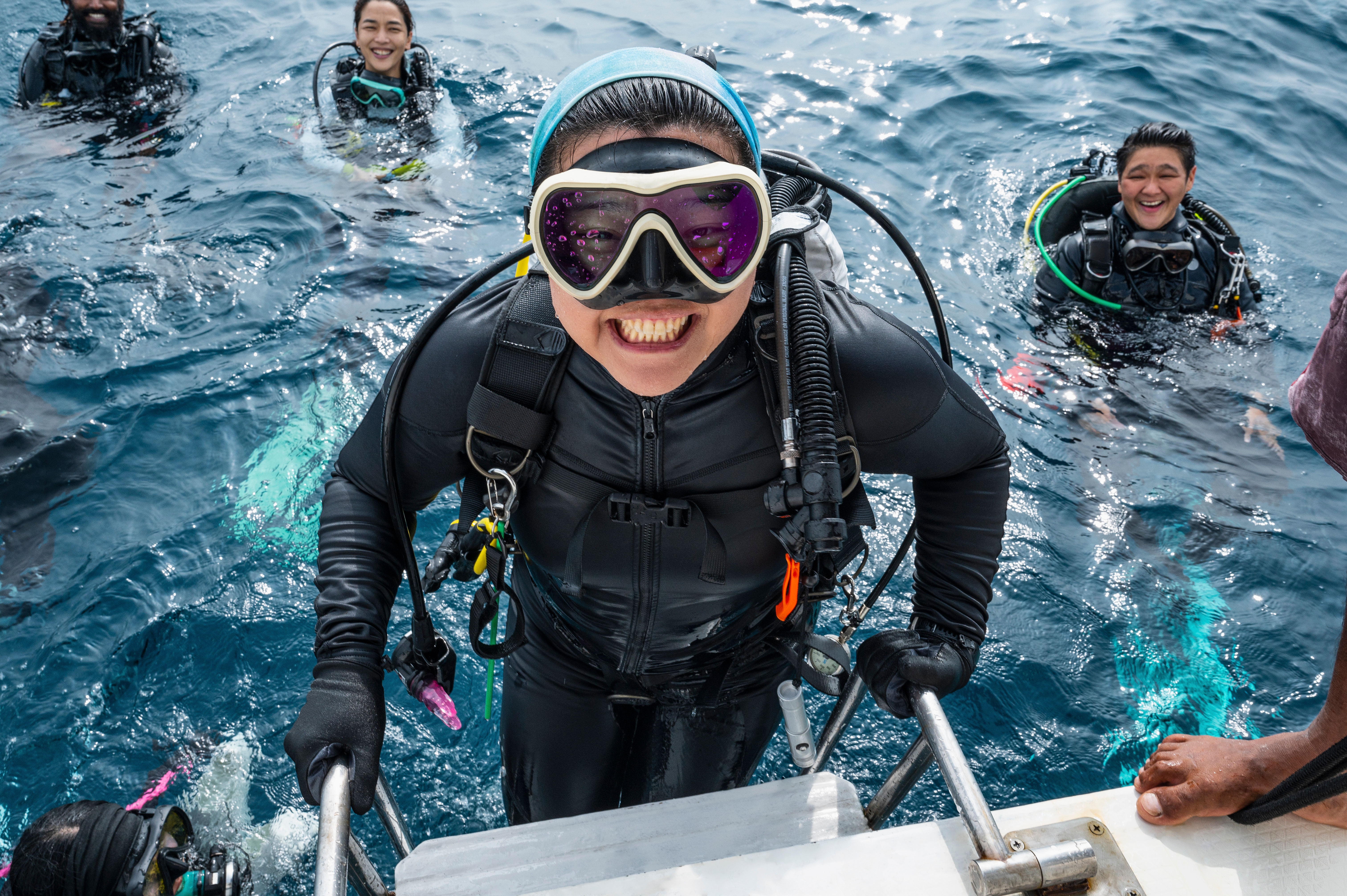 Person successful  scuba cogwheel  smiles portion    climbing a vessel  ladder; others successful  diving suits are successful  the h2o  nearby