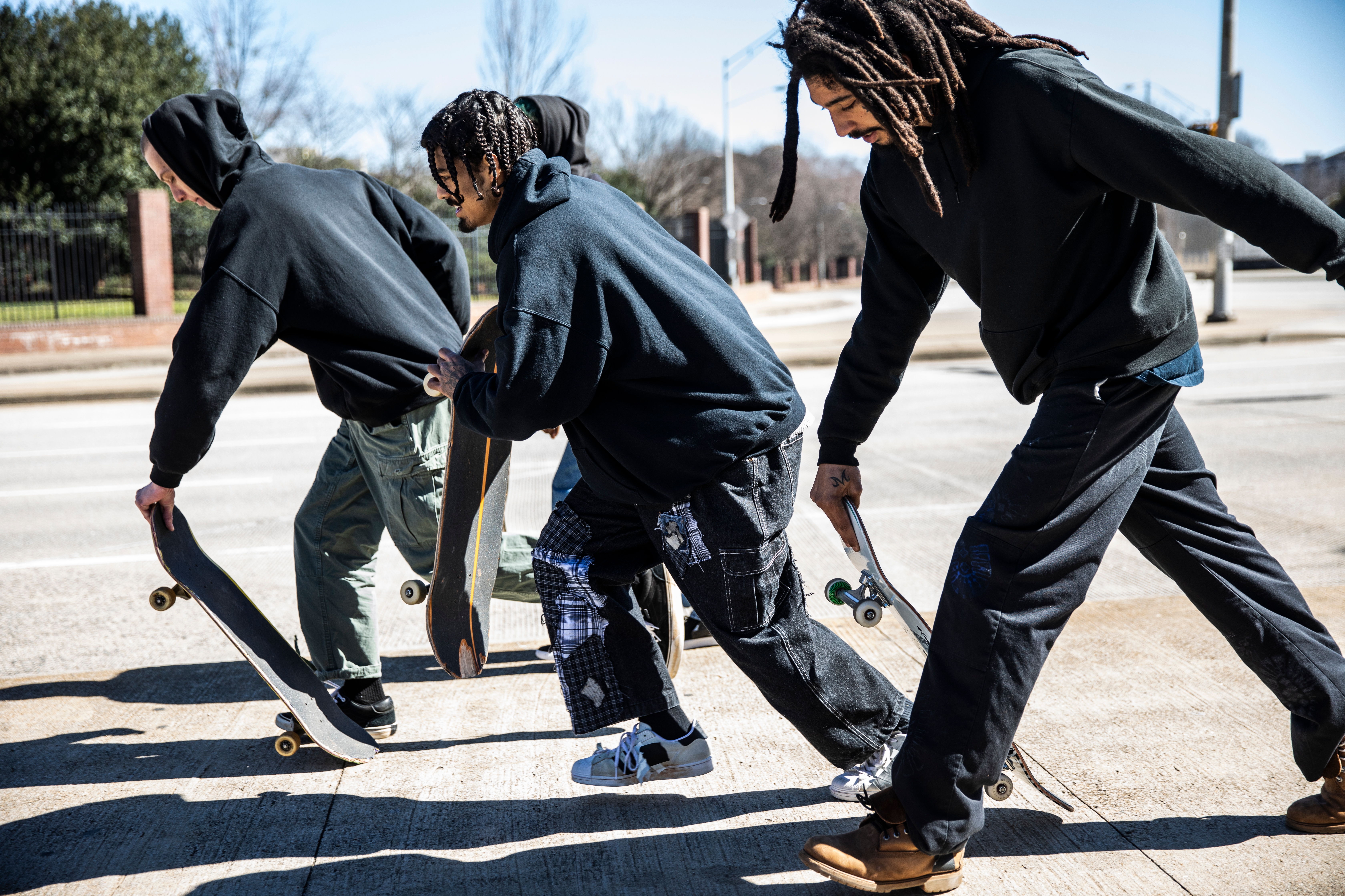 Three skateboarders successful  casual attire hole   to move. They clasp  skateboards successful  1  hand, crouching somewhat  connected  an municipality  sidewalk