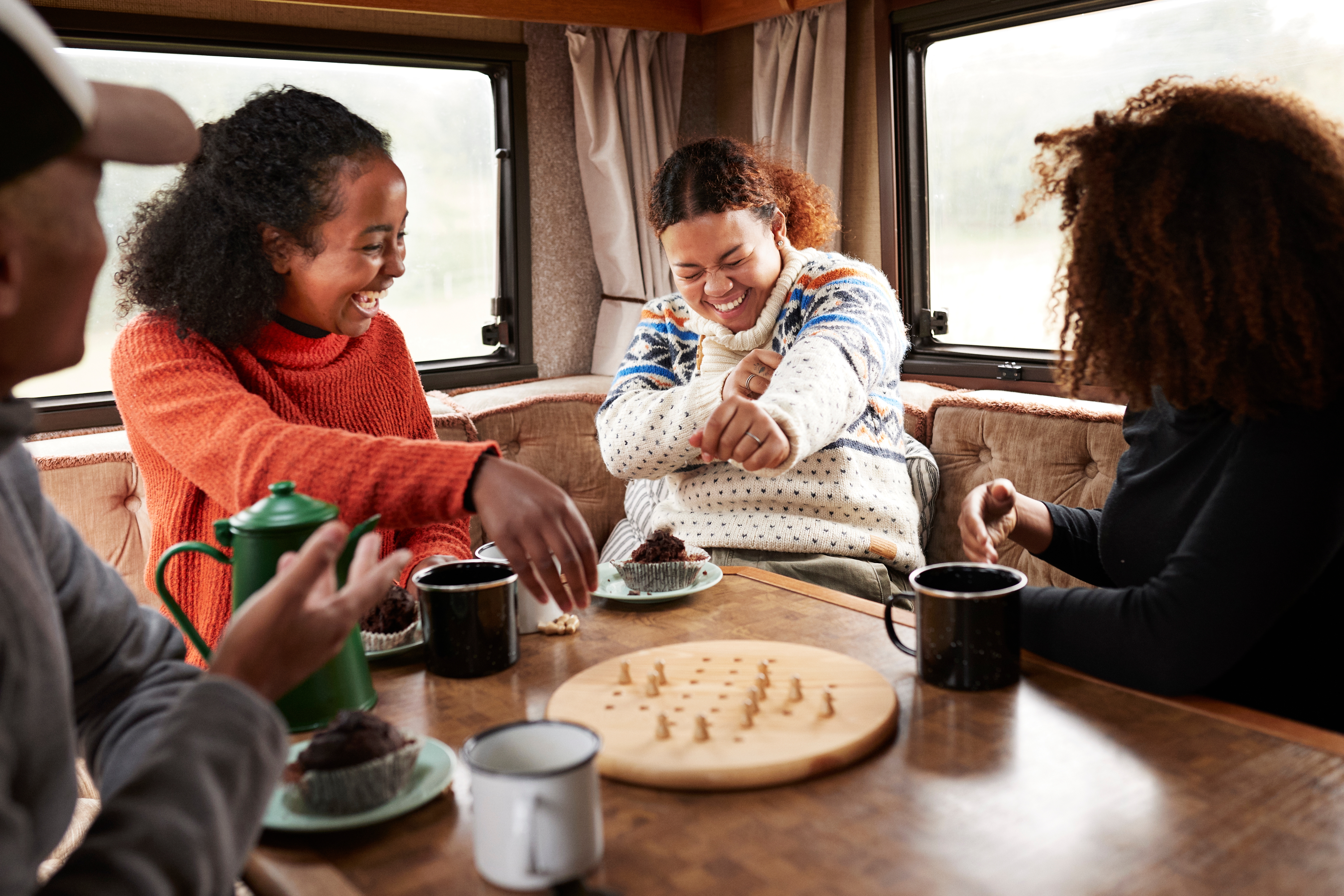 Four radical   enjoying beverage  and desserts portion    playing a committee  crippled  wrong  a cozy camper van. Smiling and engaged successful  conversation
