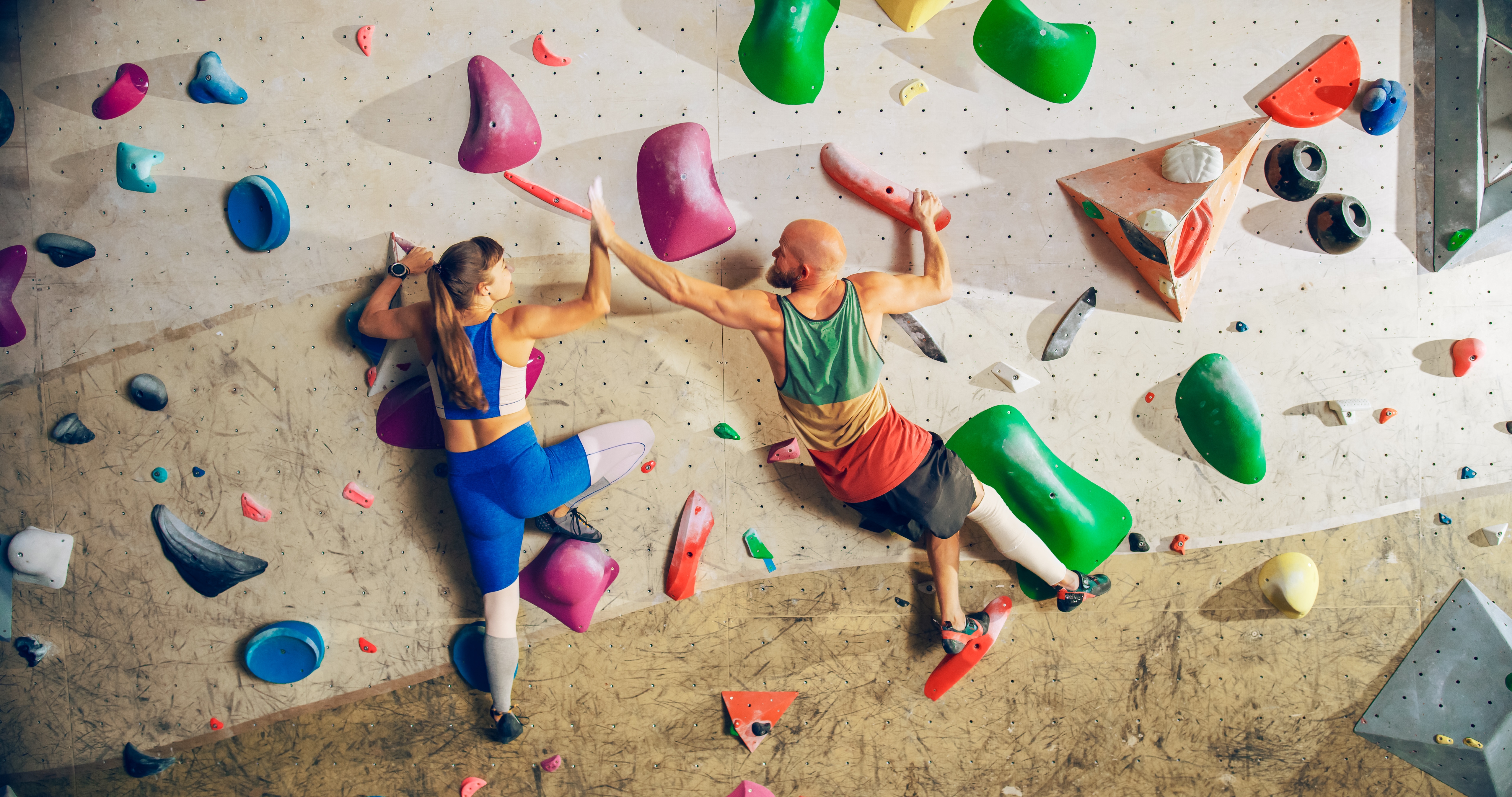 Two radical   are climbing a colorful indoor bouldering wall, wearing diversion  gear
