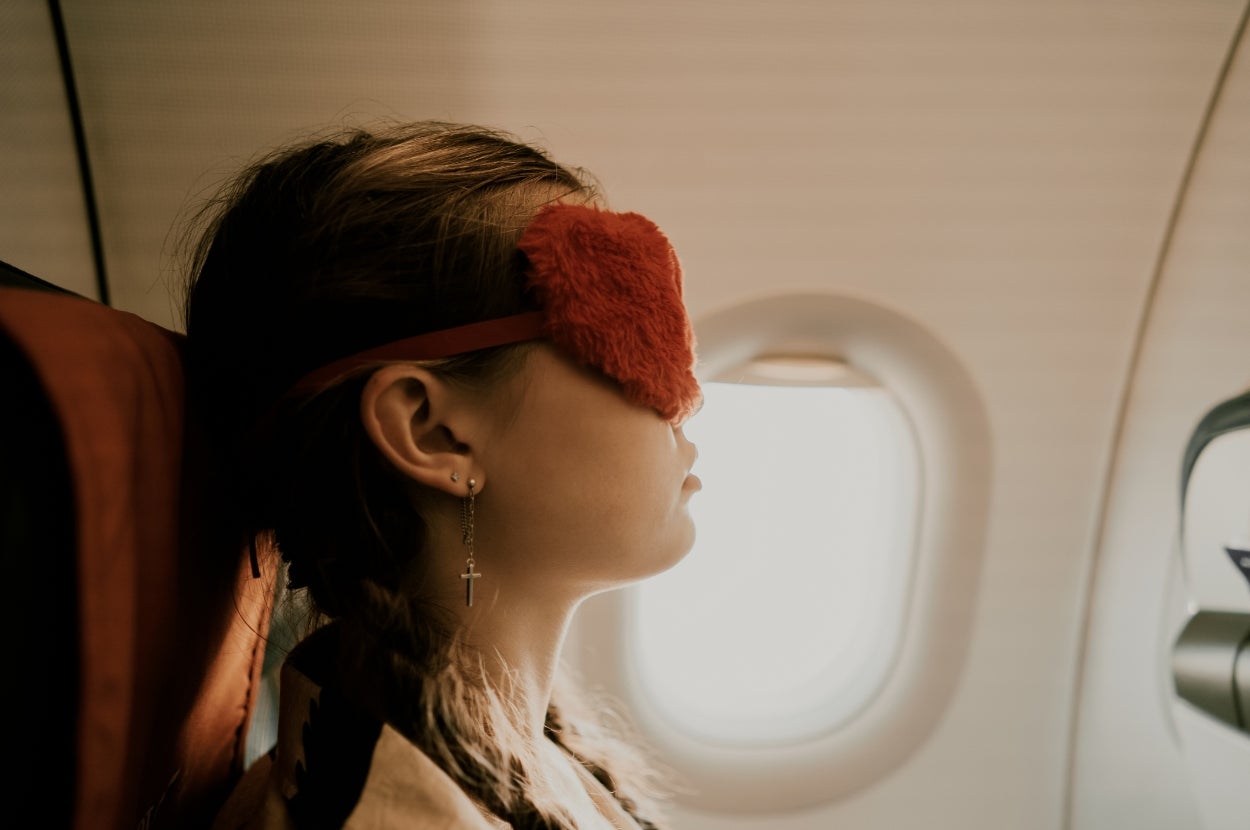 Person wearing a fluffy sleeping mask, sitting by an airplane window