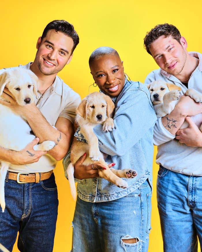 Three individuals smiling at the camera, each holding a Labrador puppy, set against a plain background