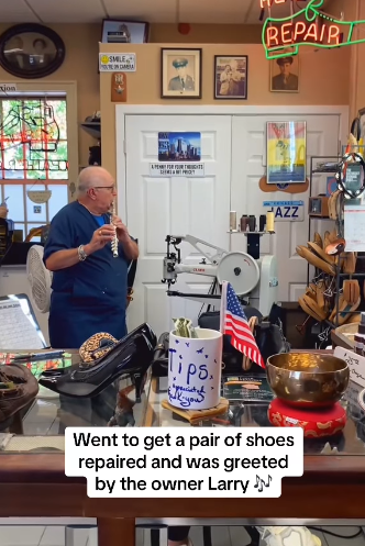 Man playing a flute successful  a footwear  repair shop, surrounded by tools. A extremity   jar and an American emblem  are connected  the counter. A motion   reads, "Smile, you're amazing."