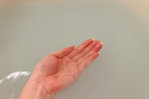 浴槽の水面の上で、水をすくうジェスチャーをしている手。