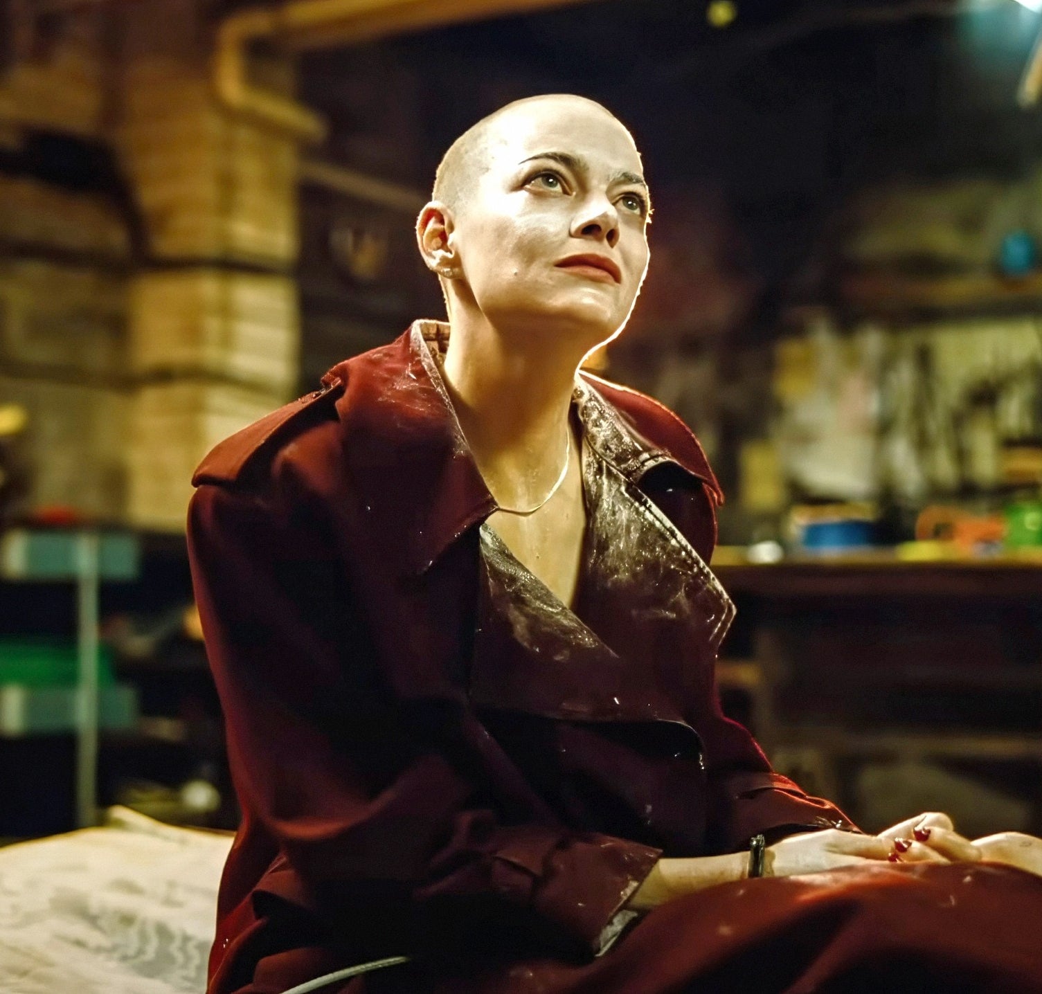 Emma with shaved head in a dark, cluttered room in a scene from "Bugonia"