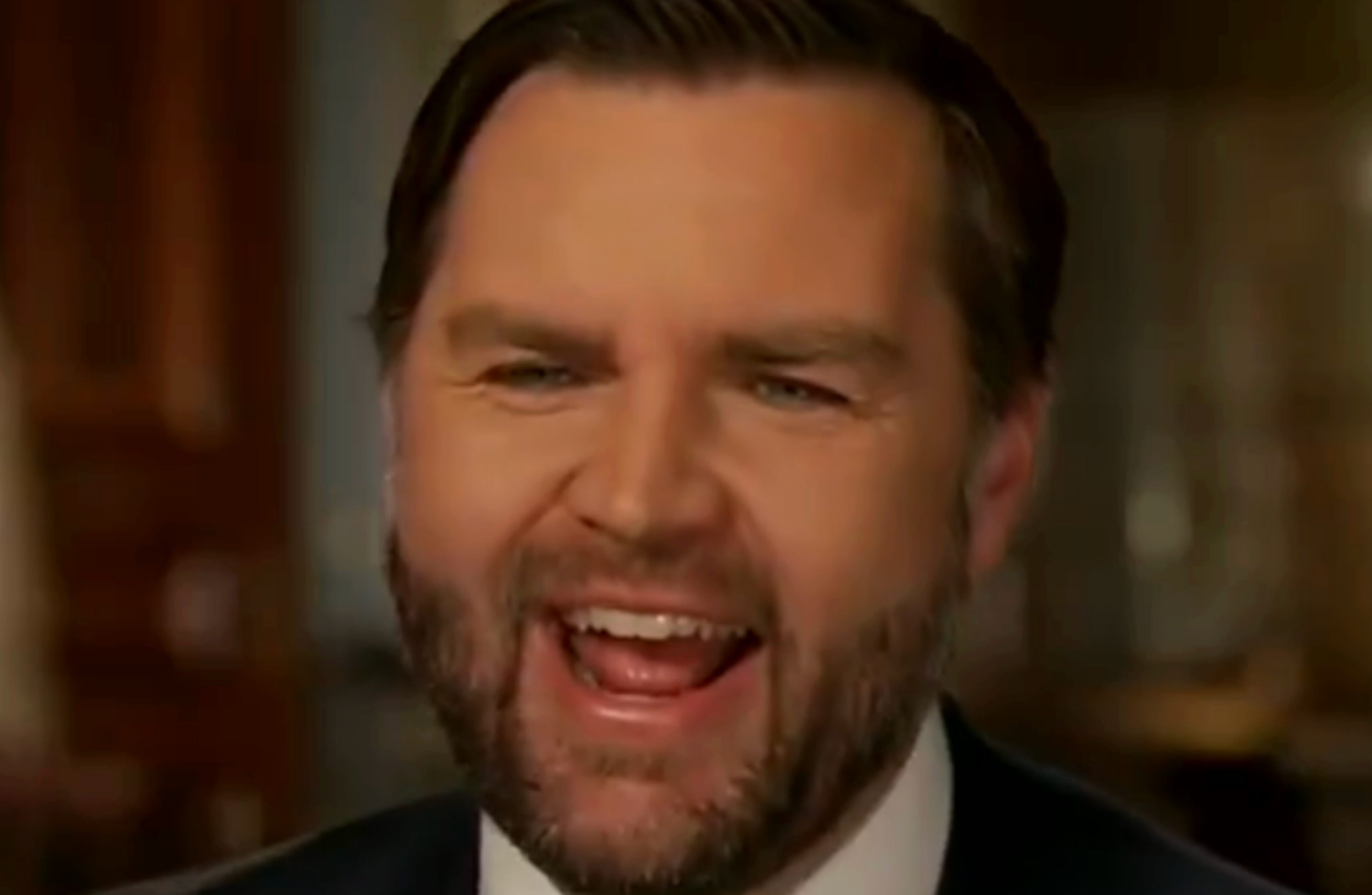 Mann i dress og slips, smilende bredt, snakker innendørs