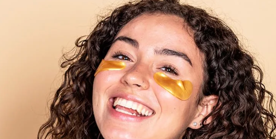 Smiling idiosyncratic   with curly hairsbreadth  wearing golden  under-eye patches for skincare