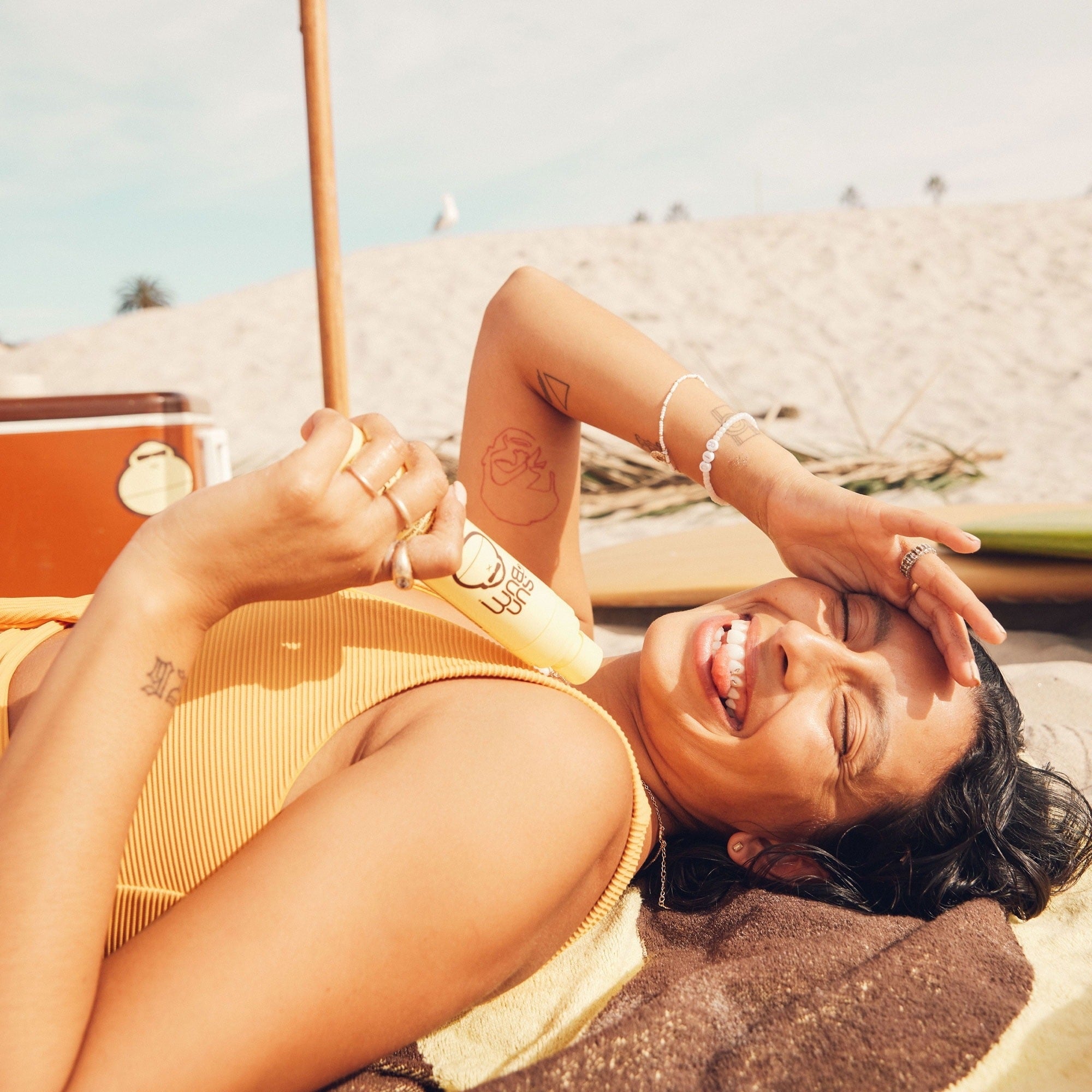 Model smiling portion    lying connected  the beach, holding a popsicle, with tattoos and casual beachwear