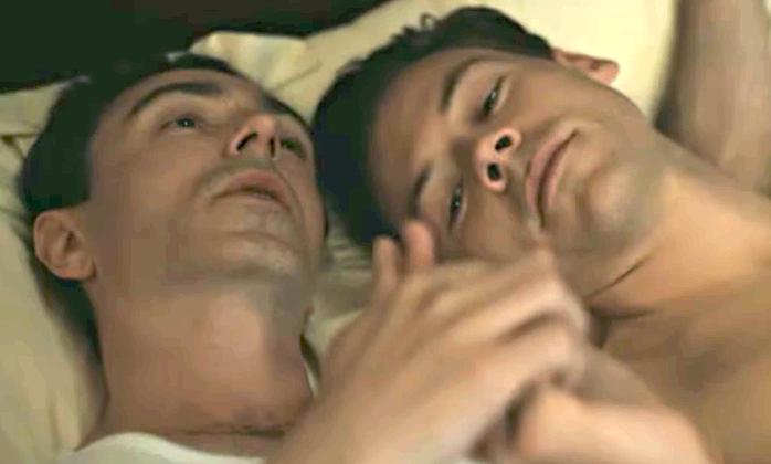 Two people lying close in bed, holding hands, gazing at each other with relaxed expressions, suggesting intimacy and connection