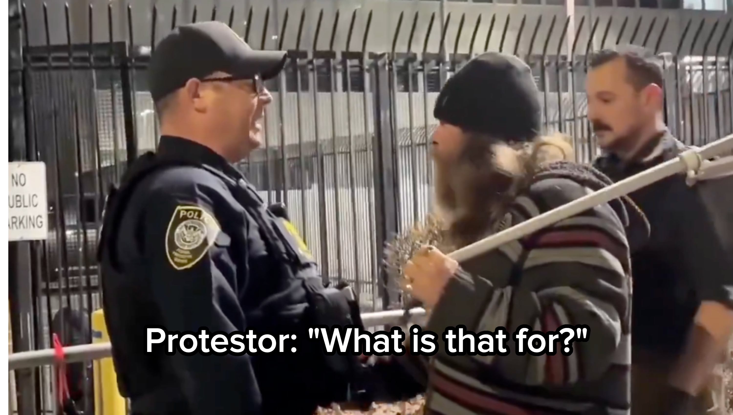 En person i stripet genser snakker med en politimann utenfor et inngjerdet område. En annen offiser står i nærheten