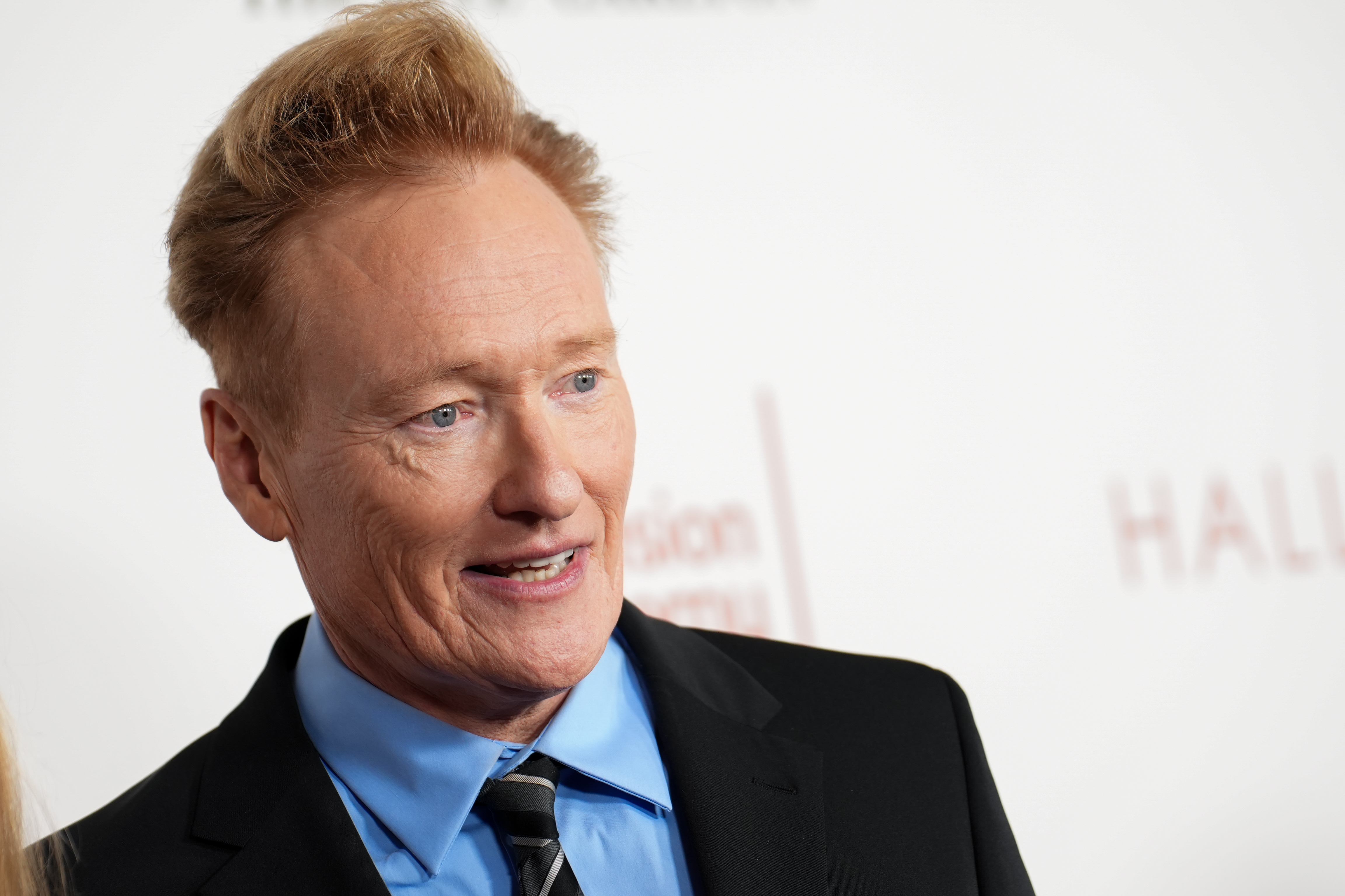 Person på et arrangement iført dress med skjorte med krage og slips, smilende