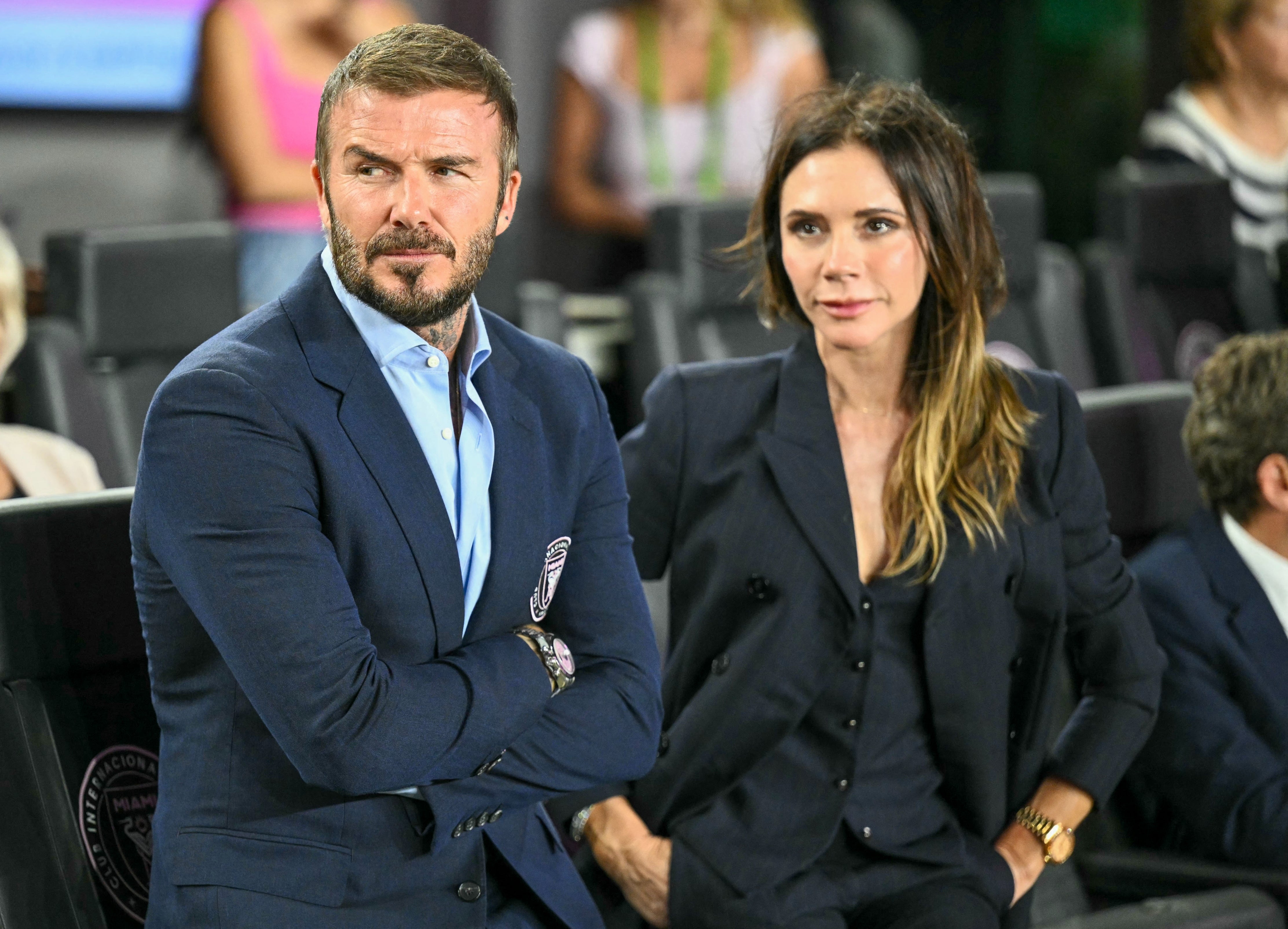 David dan Victoria Beckham dalam setelan jas berdiri berdampingan dalam suasana formal, tampil penuh perhatian
