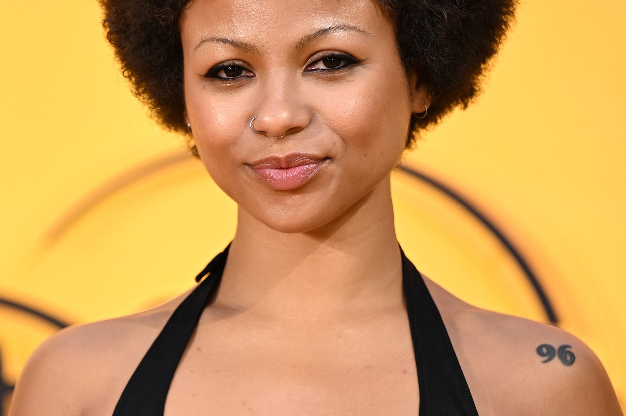 Myhala on a red carpet wearing a halter top with tattoos visible on shoulder and chest