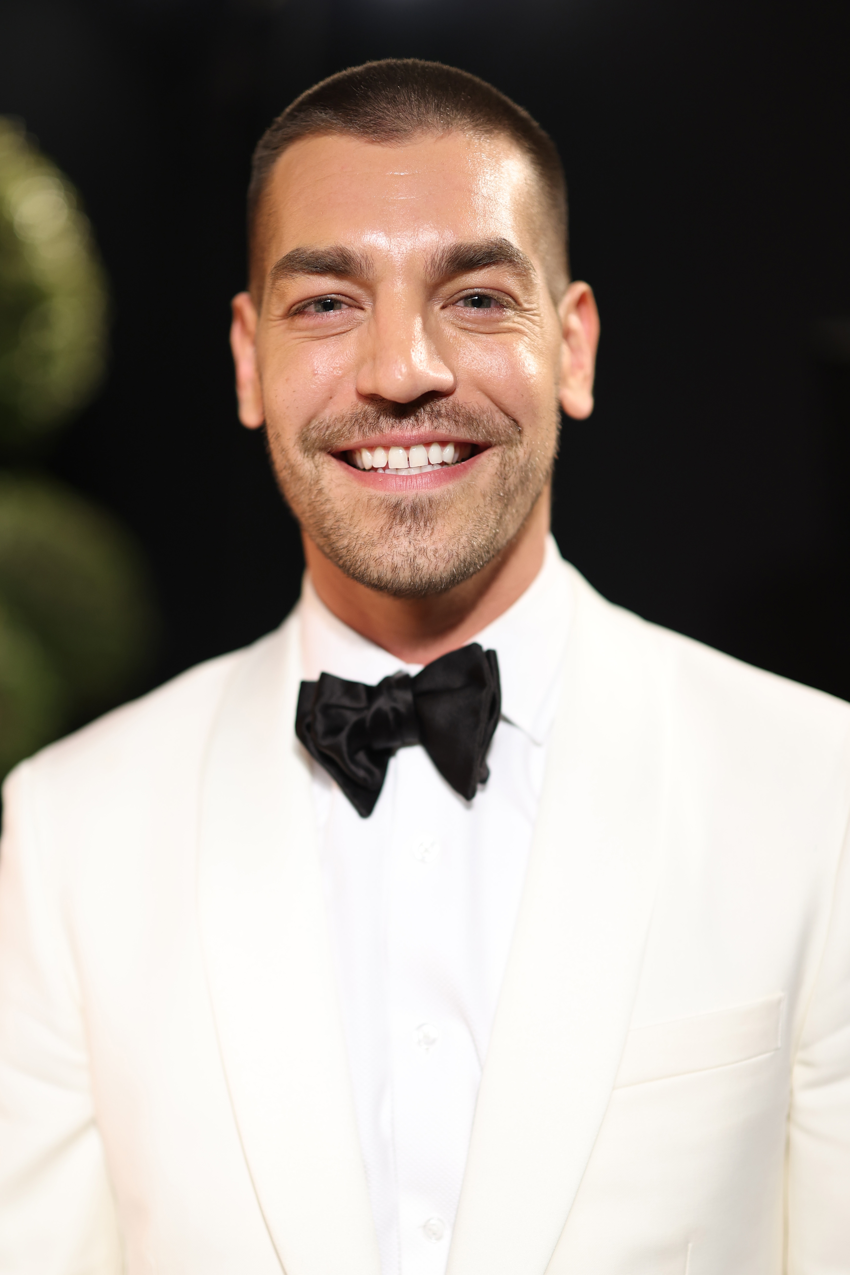 Man smiles in a white tuxedo with a black bow tie at a formal event