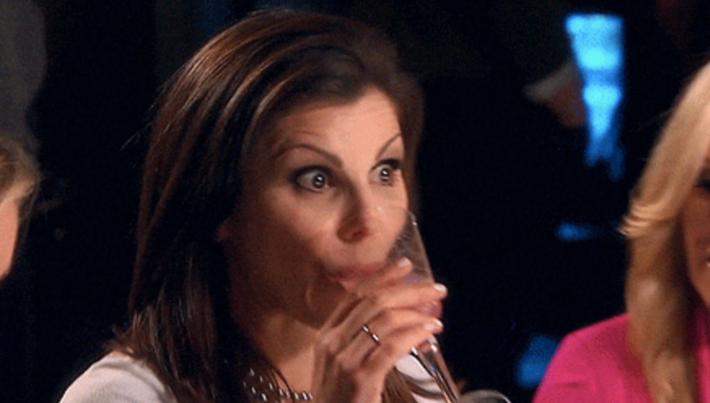 Two women astatine  a societal  gathering, 1  sipping from a solid  with a amazed  expression, portion    the different   is successful  conversation