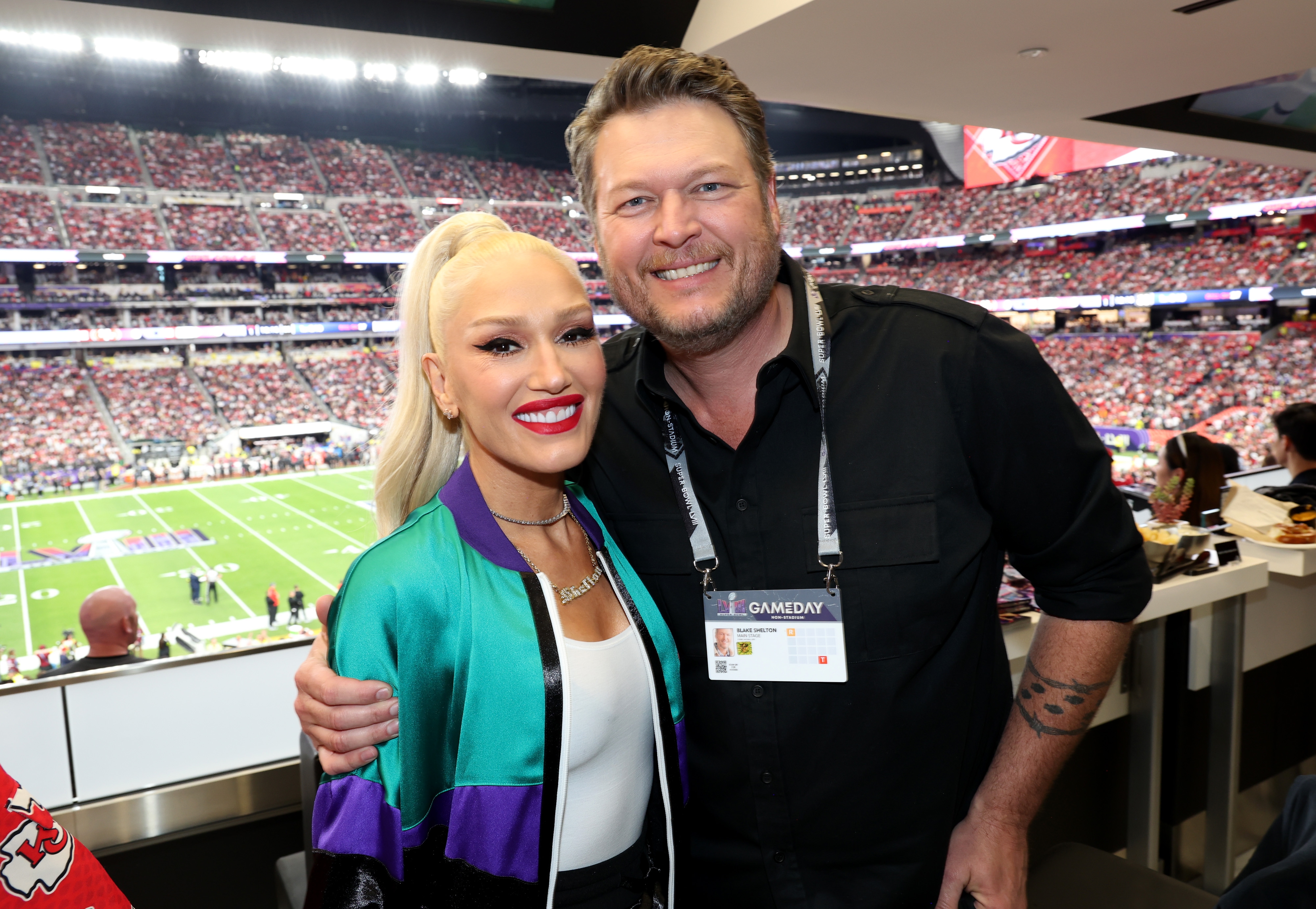 Gwen Stefani and Blake Shelton smiling successful  a stadium suite, with 1  wearing a retro sports overgarment   and the different   successful  casual attire. Football tract  disposable   successful  the background