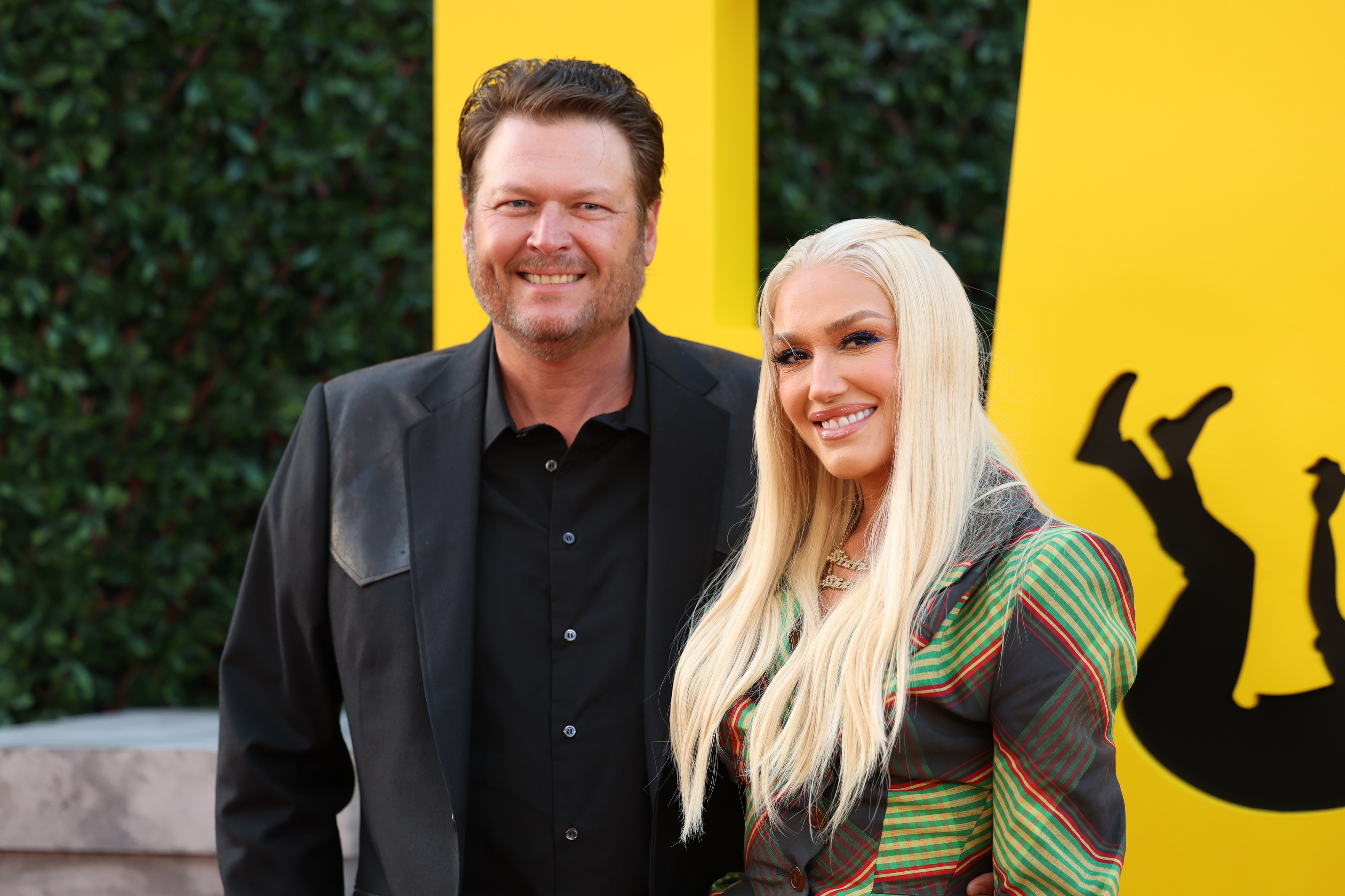 Blake Shelton and Gwen Stefani smiling astatine  a media event; the pistillate   wears a stylish striped overgarment   with salient  shoulders