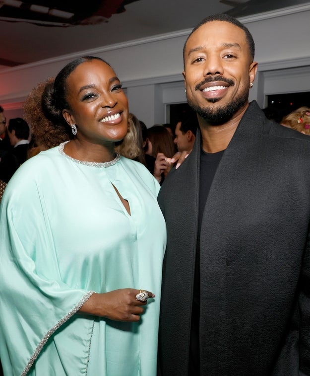 Two radical   smiling astatine  an event. The idiosyncratic   connected  the near  wears an elegant draped dress, and the idiosyncratic   connected  the close    wears a sharp, acheronian  coat