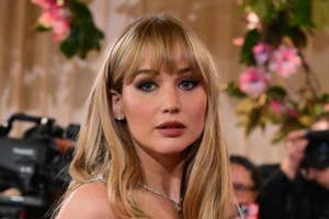 Jennifer in floral-patterned sheer outfit with matching cape on red carpet, surrounded by photographers and greenery