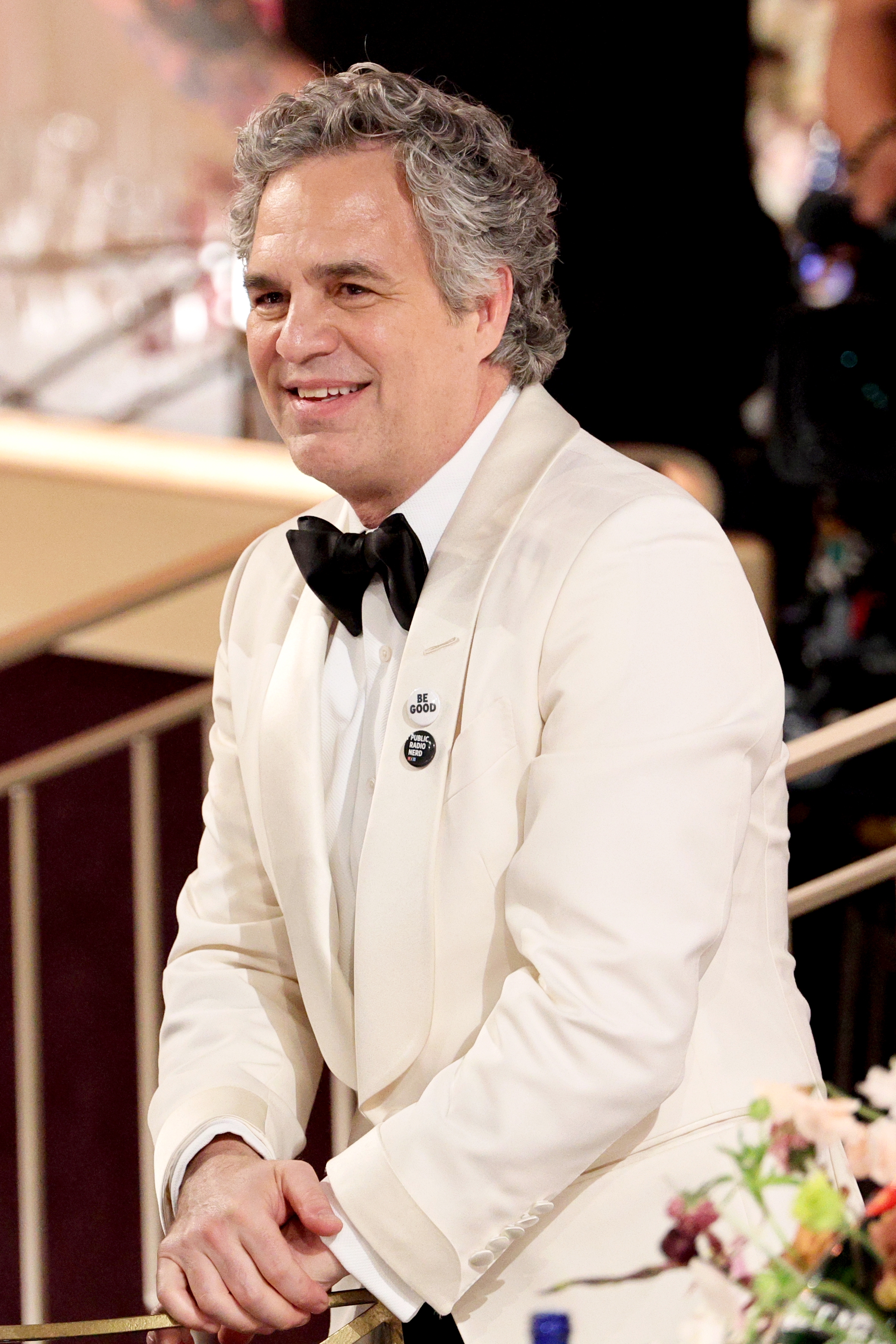 Mark Ruffalo wearing a tuxedo smiles astatine an event, with a pin connected their lapel