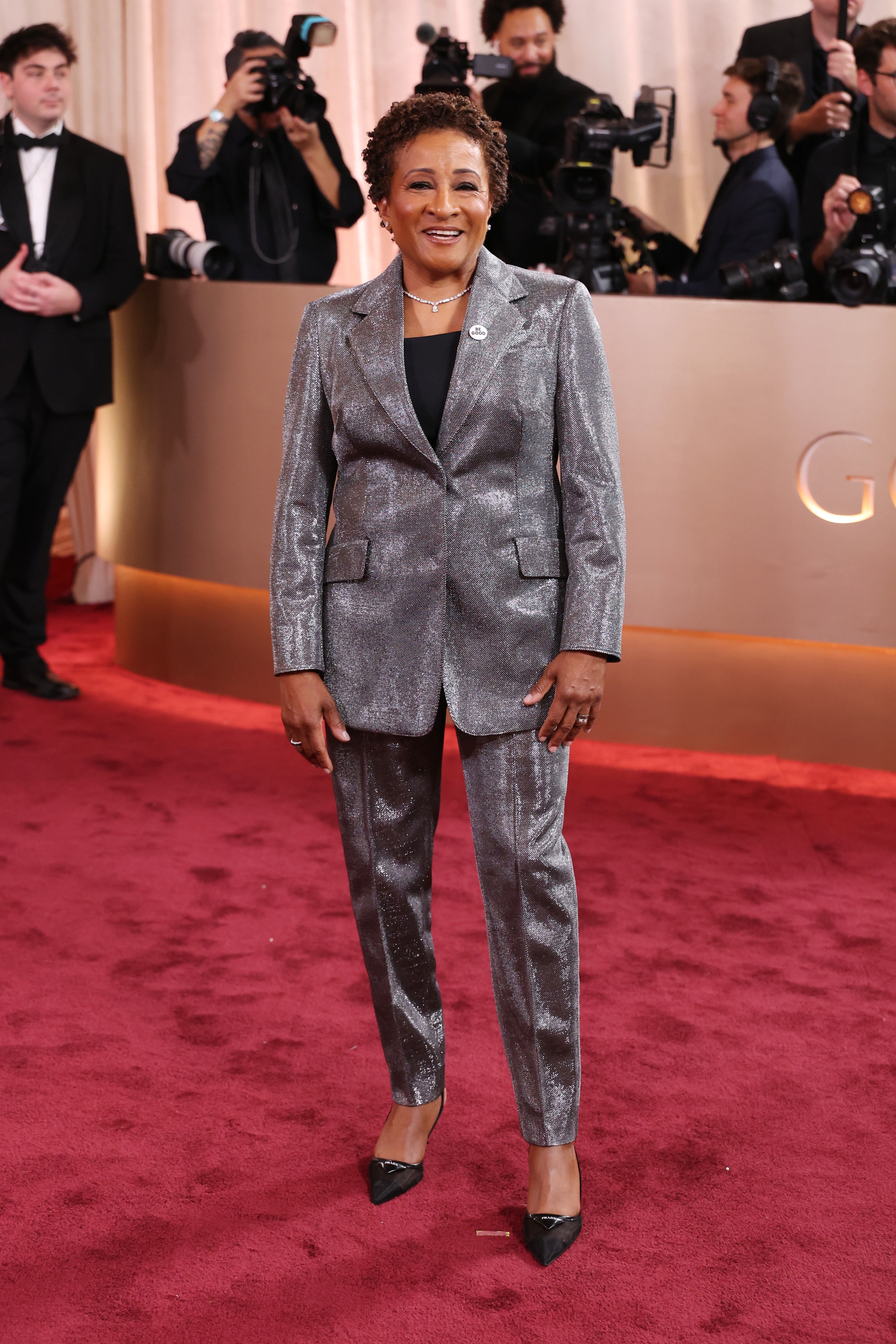 Celebrity on the red carpet wearing a shimmering suit, posing for photographers in the background