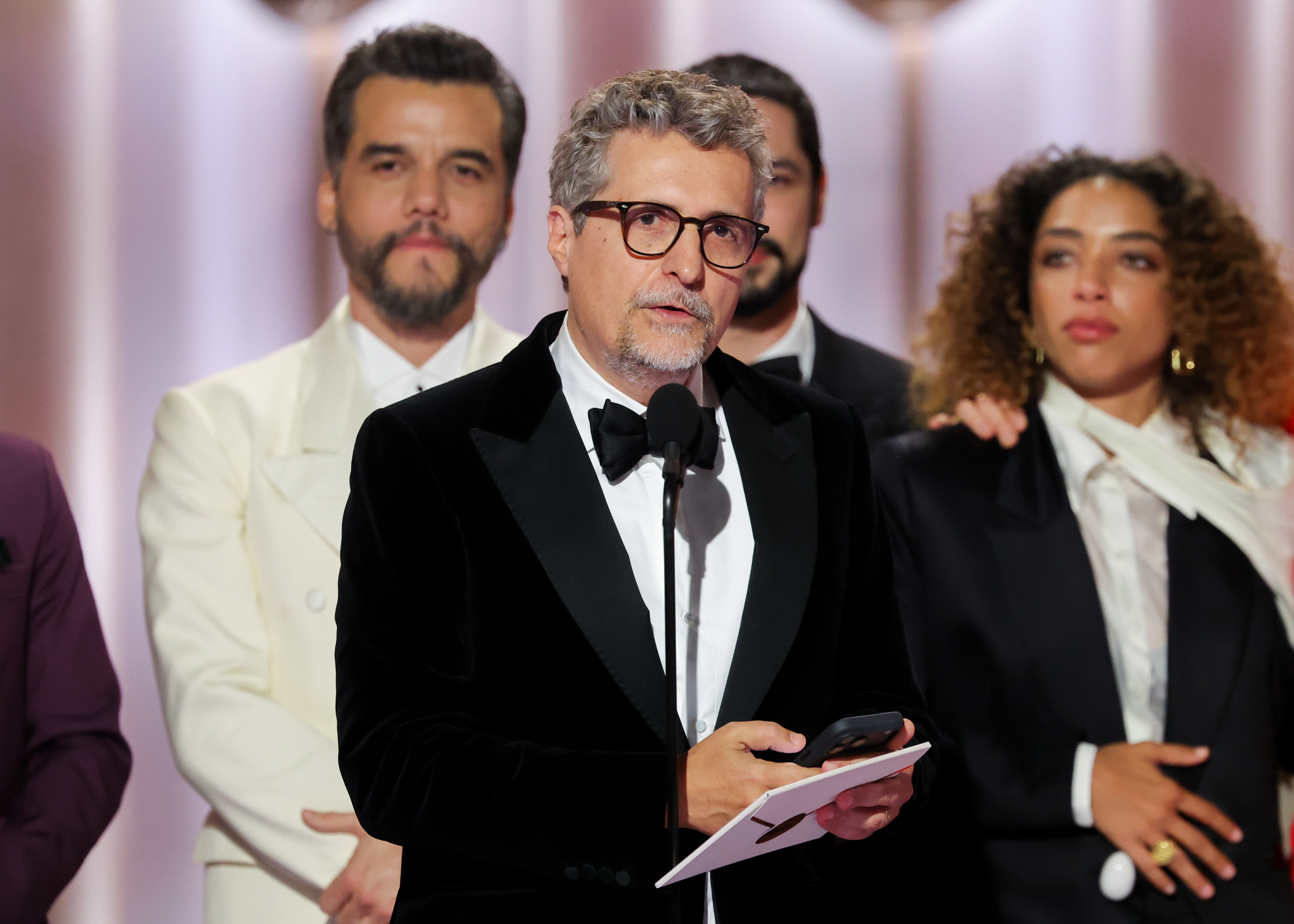 Kleber Mendonça Filho stands connected stage, speaking into a microphone portion holding a paper, astatine the Golden Globes