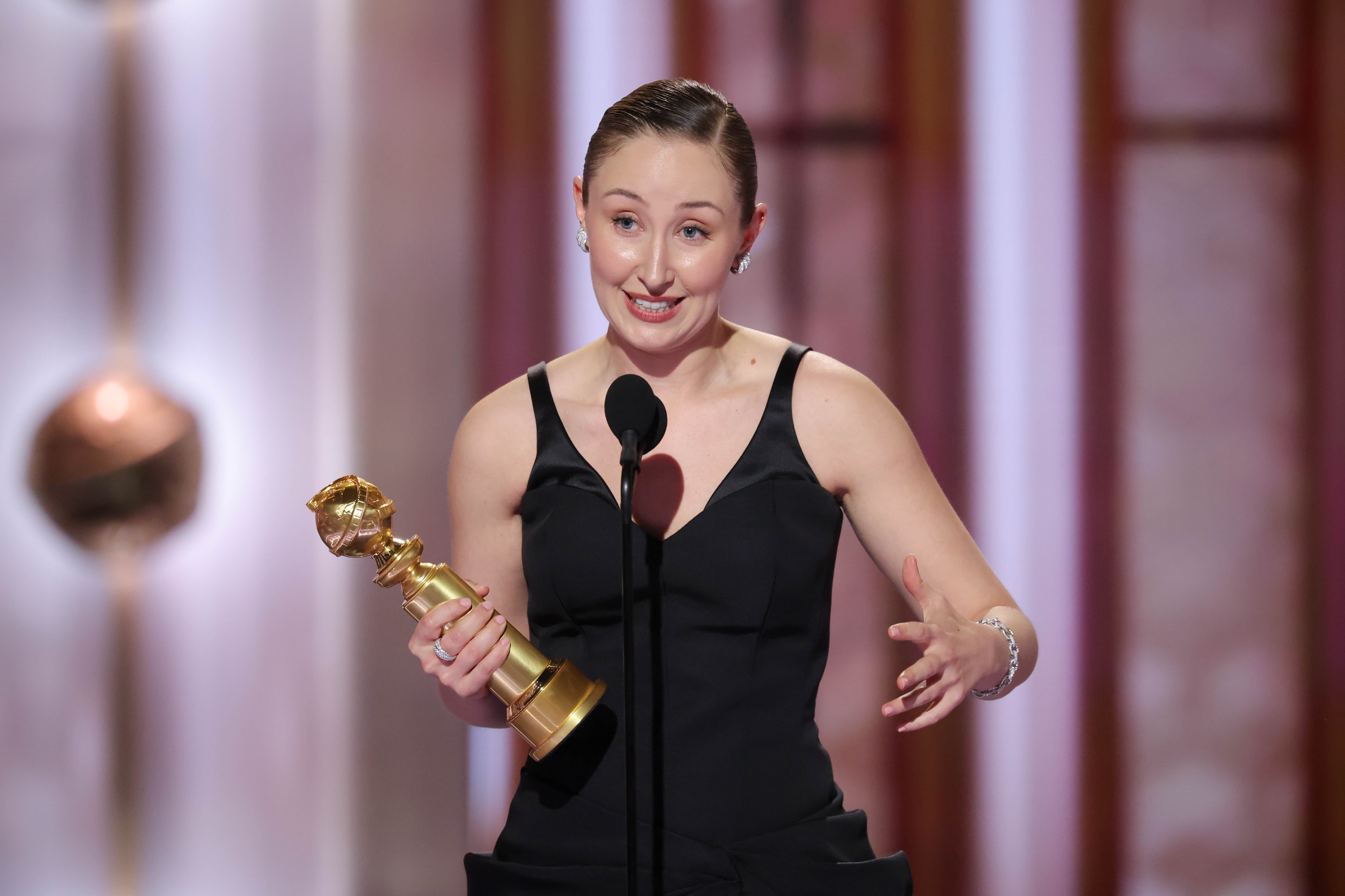 Jeg vet ikke hvem dette er, men de står på scenen og holder en pris, iført en elegant ermeløs svart kjole og snakker inn i en mikrofon