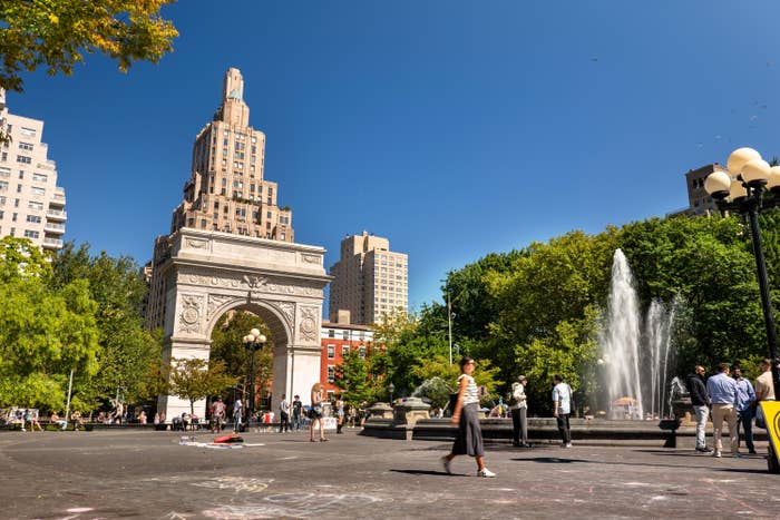 Orang-orang berjalan di dekat air mancur dan Washington Square Arch di taman kota yang sibuk