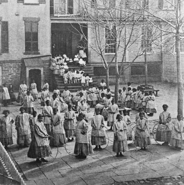 Foto bersejarah gadis-gadis muda dengan celemek bermain dengan lingkaran dan tali di halaman panti asuhan, tahun 1880-an