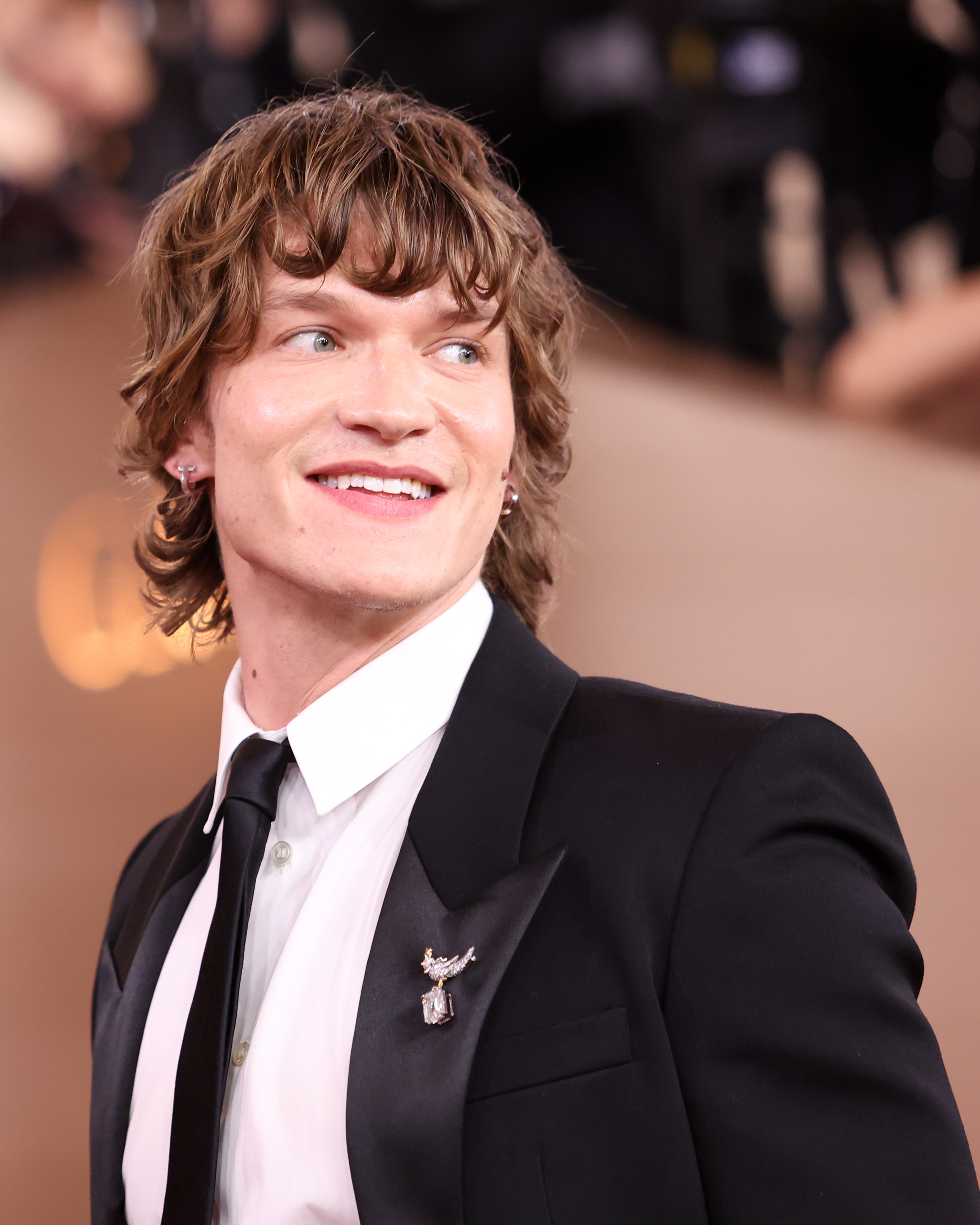 Person i dress med en brosje på en formell begivenhets røde løper, ser sidelengs og smiler