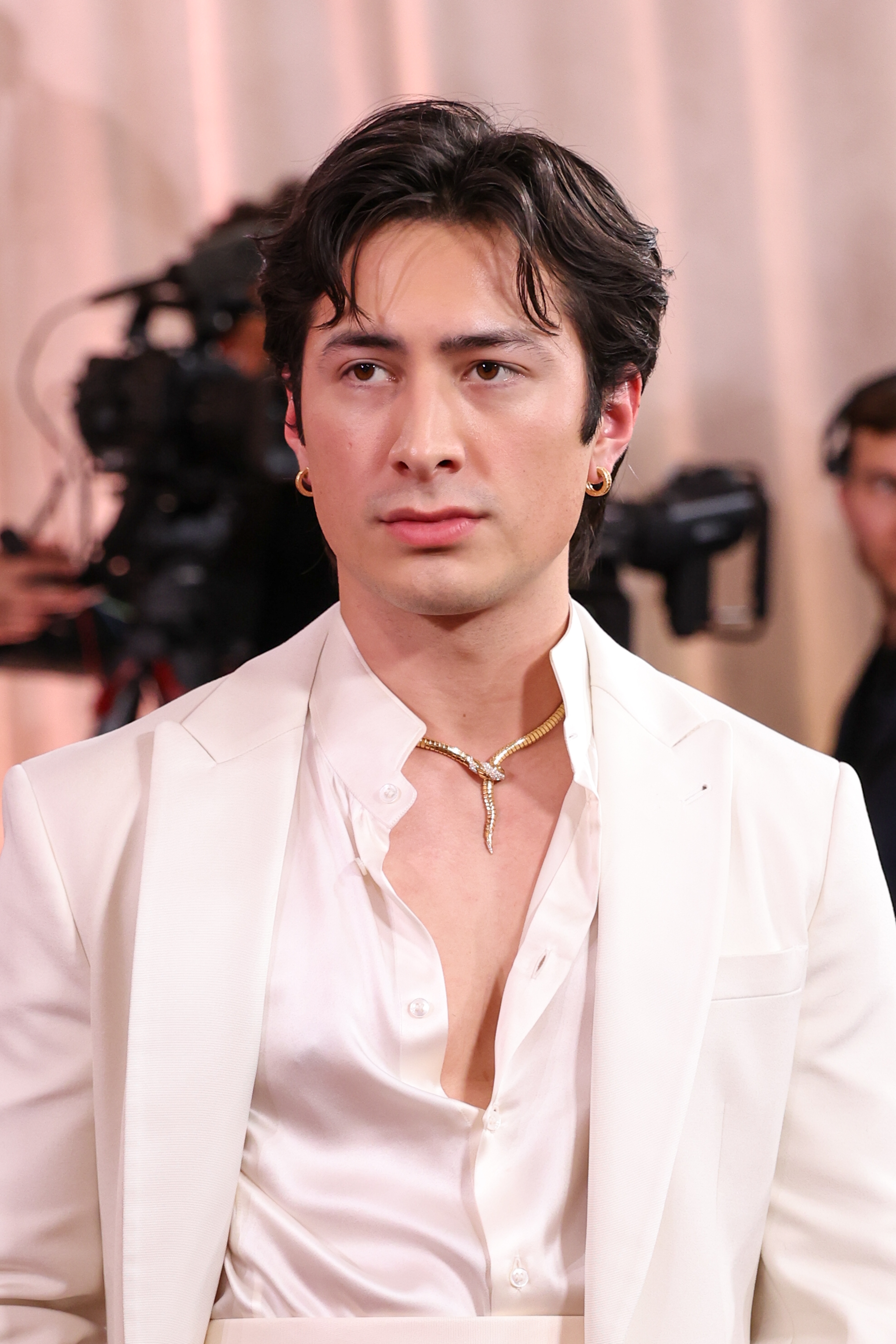 Person i elegant hvit dress med åpen skjorte og gullkjede på en rød løper