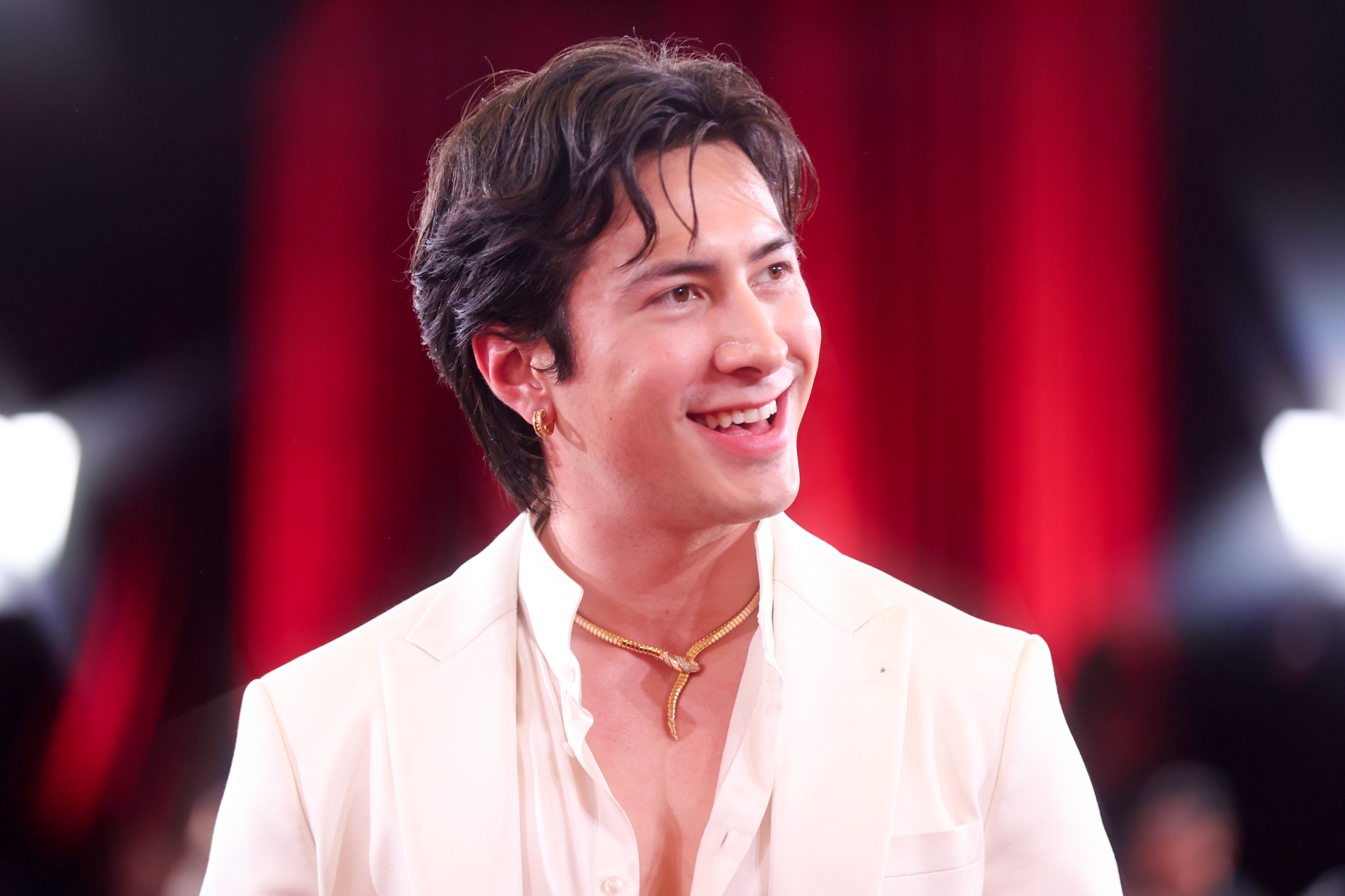 Person som smiler på rød løper, iført en lys dress og et gullkjede