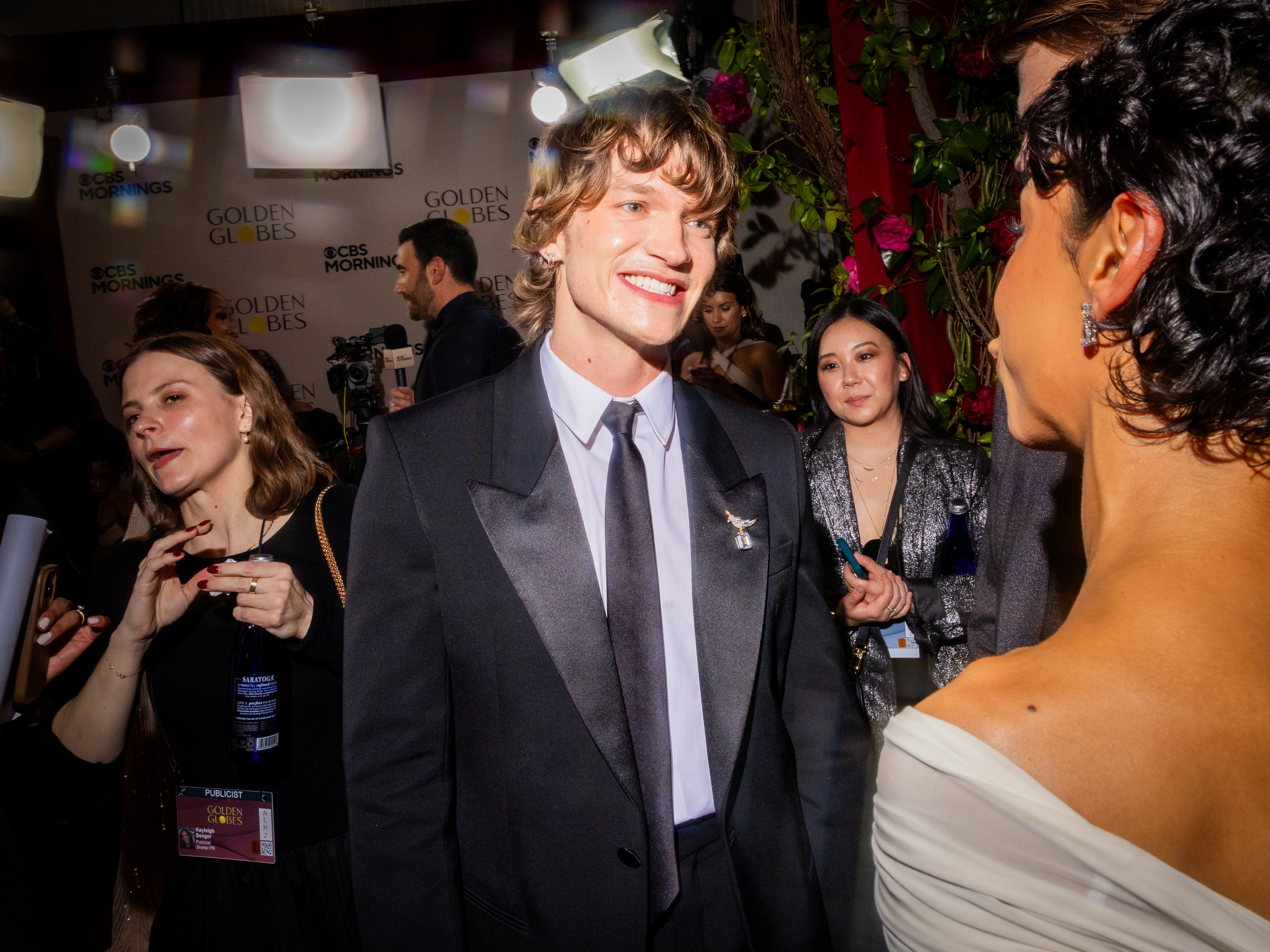 En person i dress smiler til noen på en rød løper-arrangement, omgitt av deltakere og fotografer i bakgrunnen