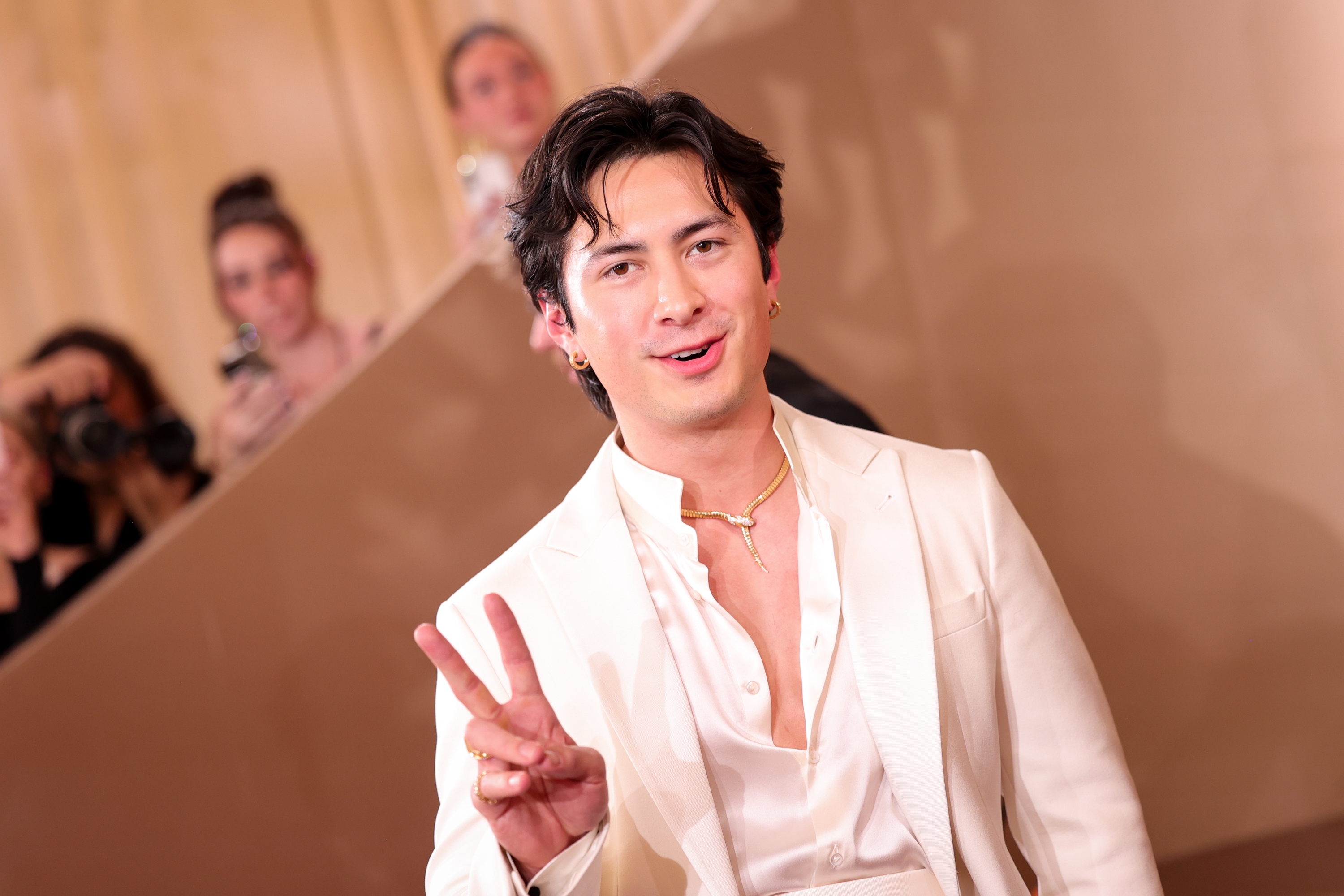 Person i hvit dress blinker med et fredsskilt på en rød løper, med fotografer i bakgrunnen som fanger øyeblikket