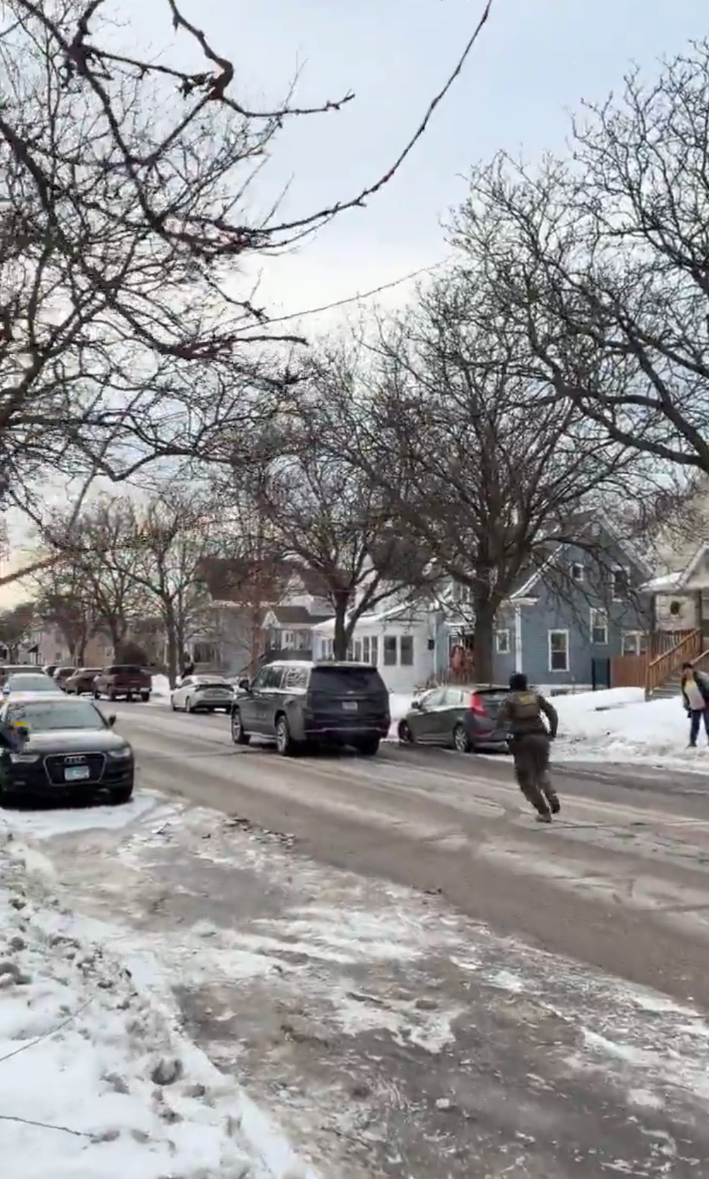 Person løper på snødekt gate med biler parkert langs siden og nakne trær langs veien, noe som indikerer en kald vinterdag i et nabolag