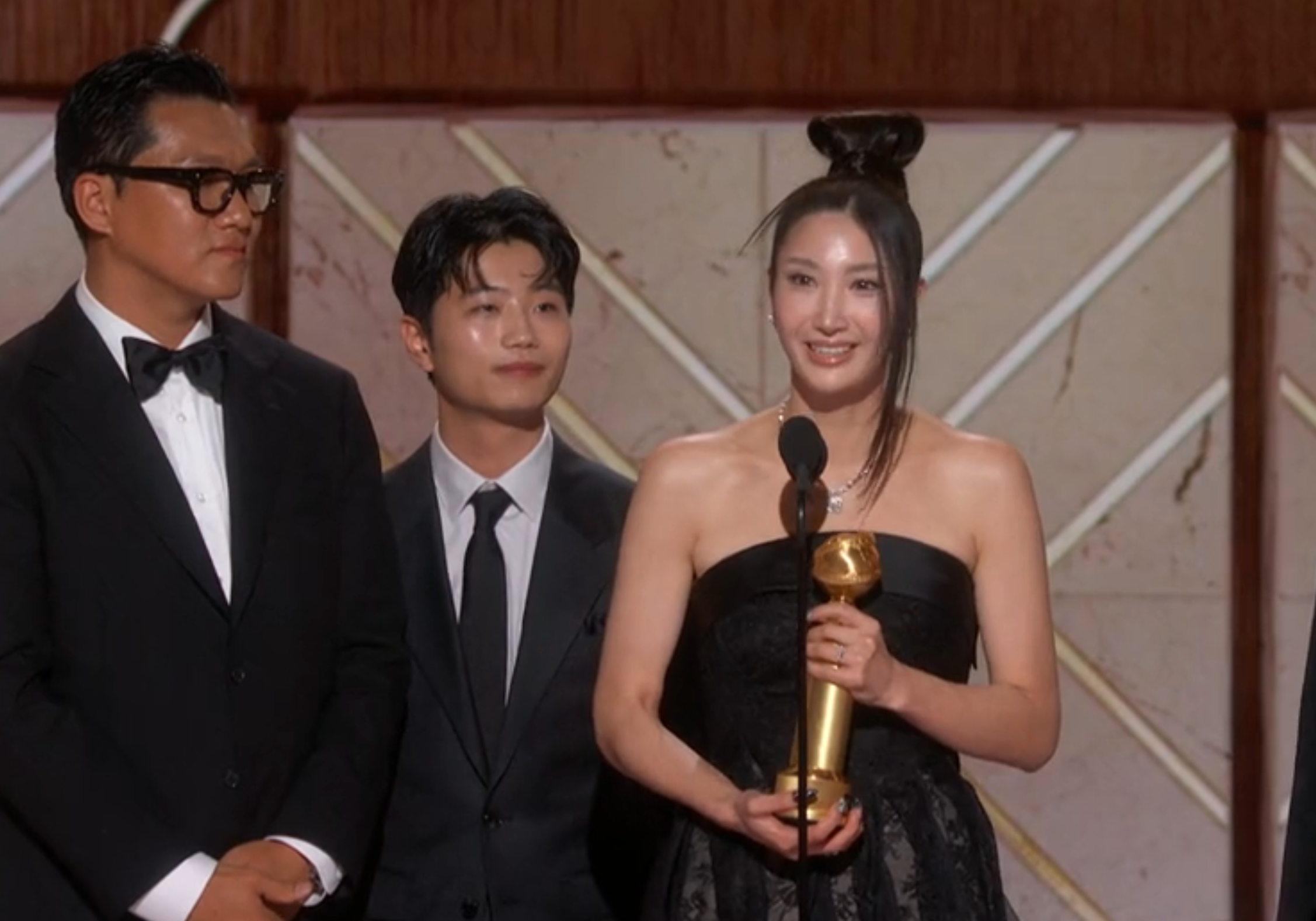 Three individuals successful  ceremonial  deterioration  connected  stage, 1  pistillate   holding a trophy and speaking into a microphone